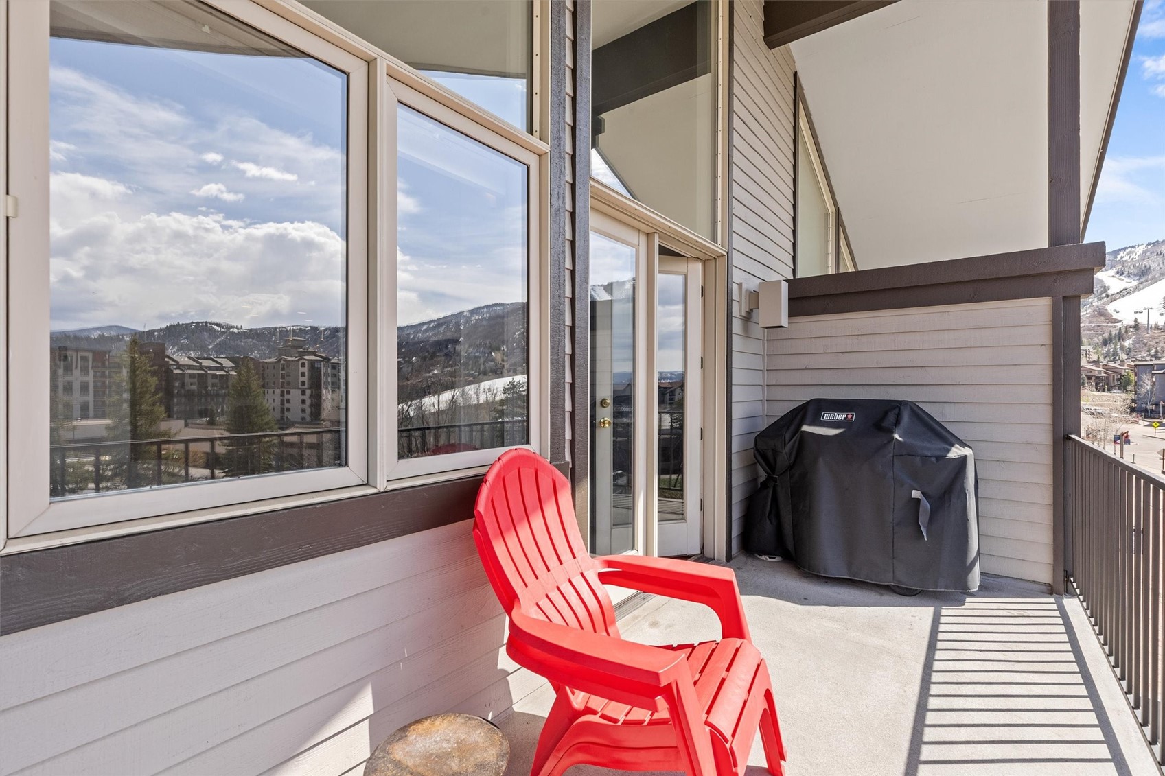 Condo balcony with red Adirondack chairs, a covered grill, and mountain views.