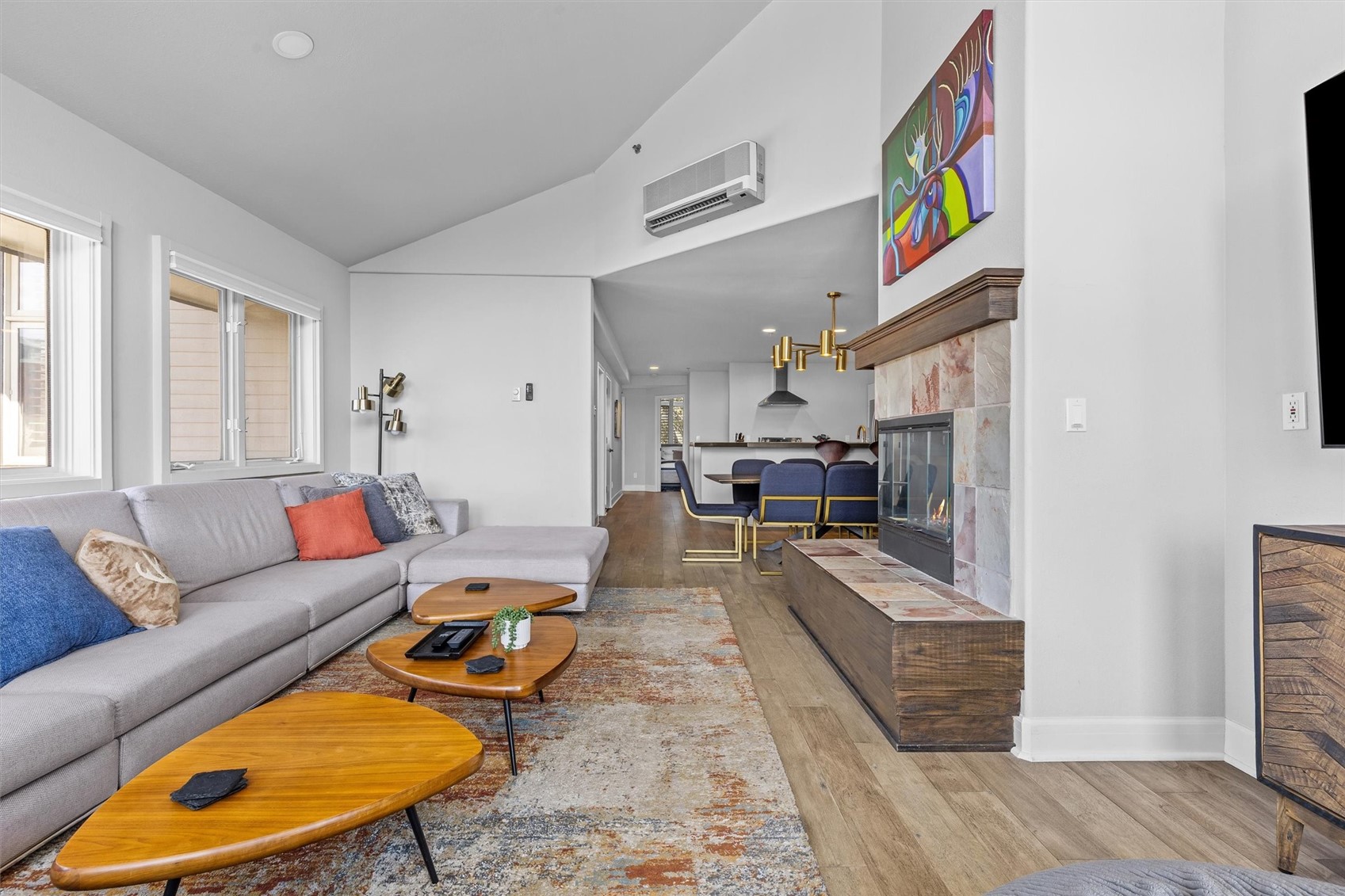 Open-plan living room with a gray sectional, stone fireplace, and dining area beyond.