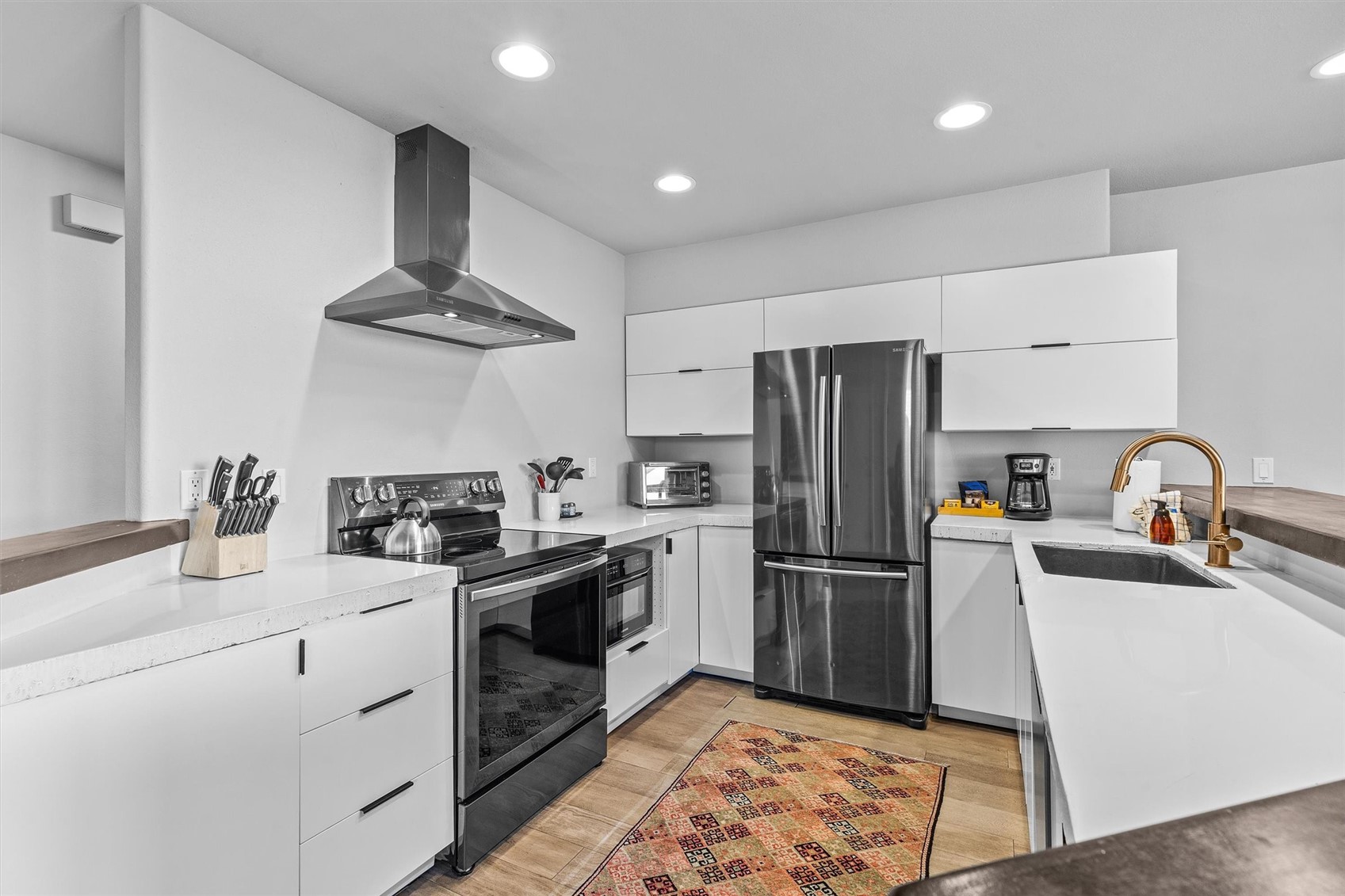 Modern kitchen with white cabinetry, stainless steel appliances, and a patterned runner rug.
