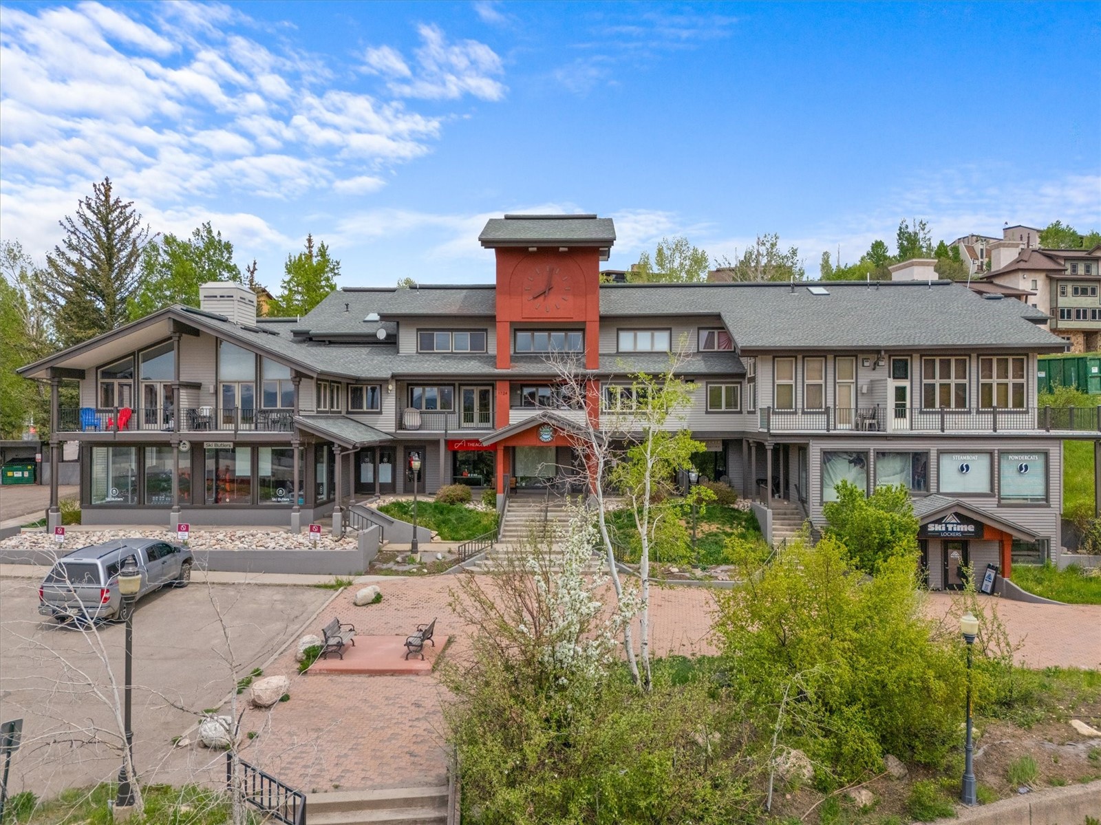 Multi-unit building with a red clock tower, storefronts, balconies, and a landscaped courtyard.