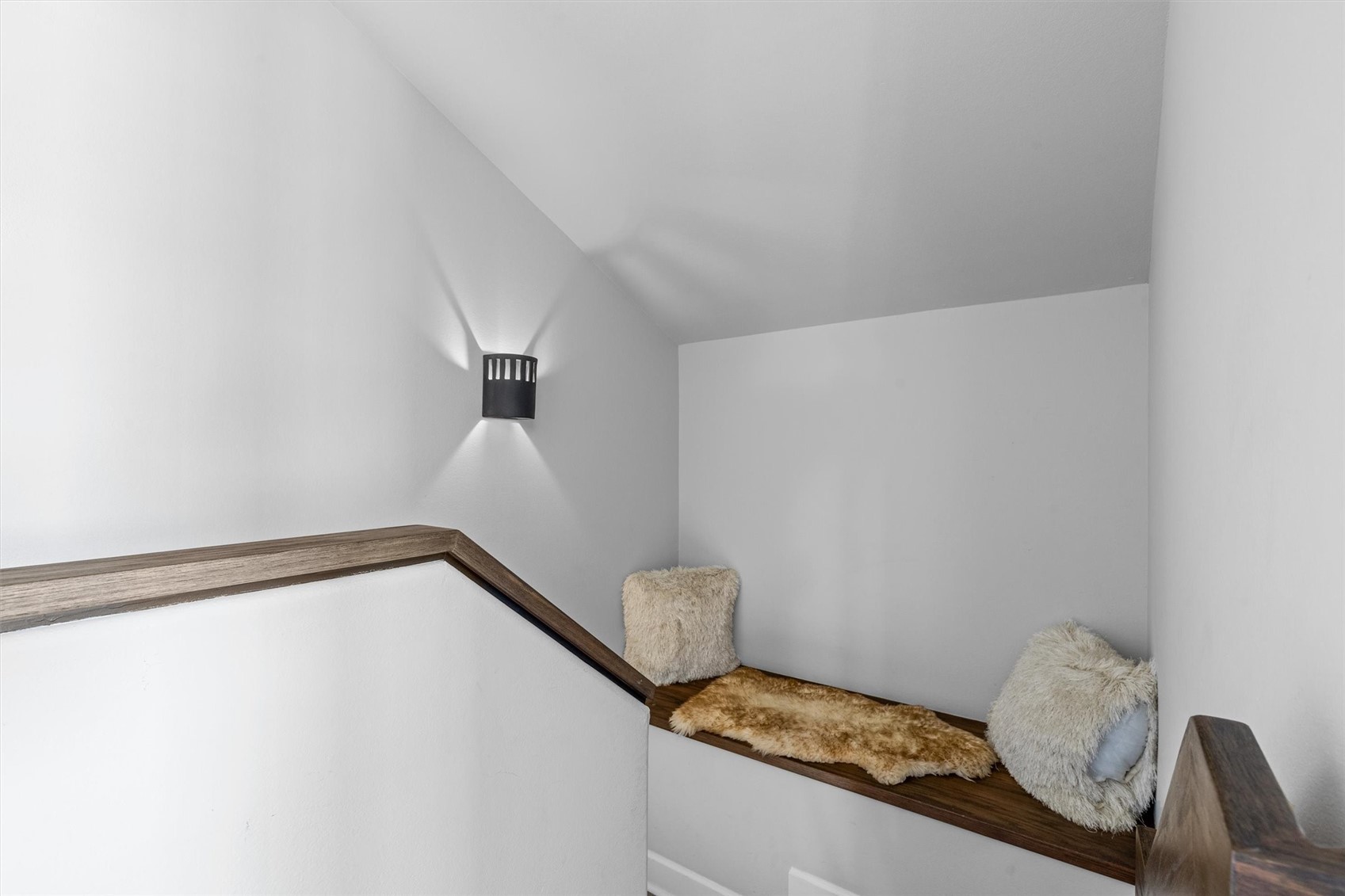 Stair landing with a built-in wood bench, fluffy cushions, a fur throw, and a wall sconce.