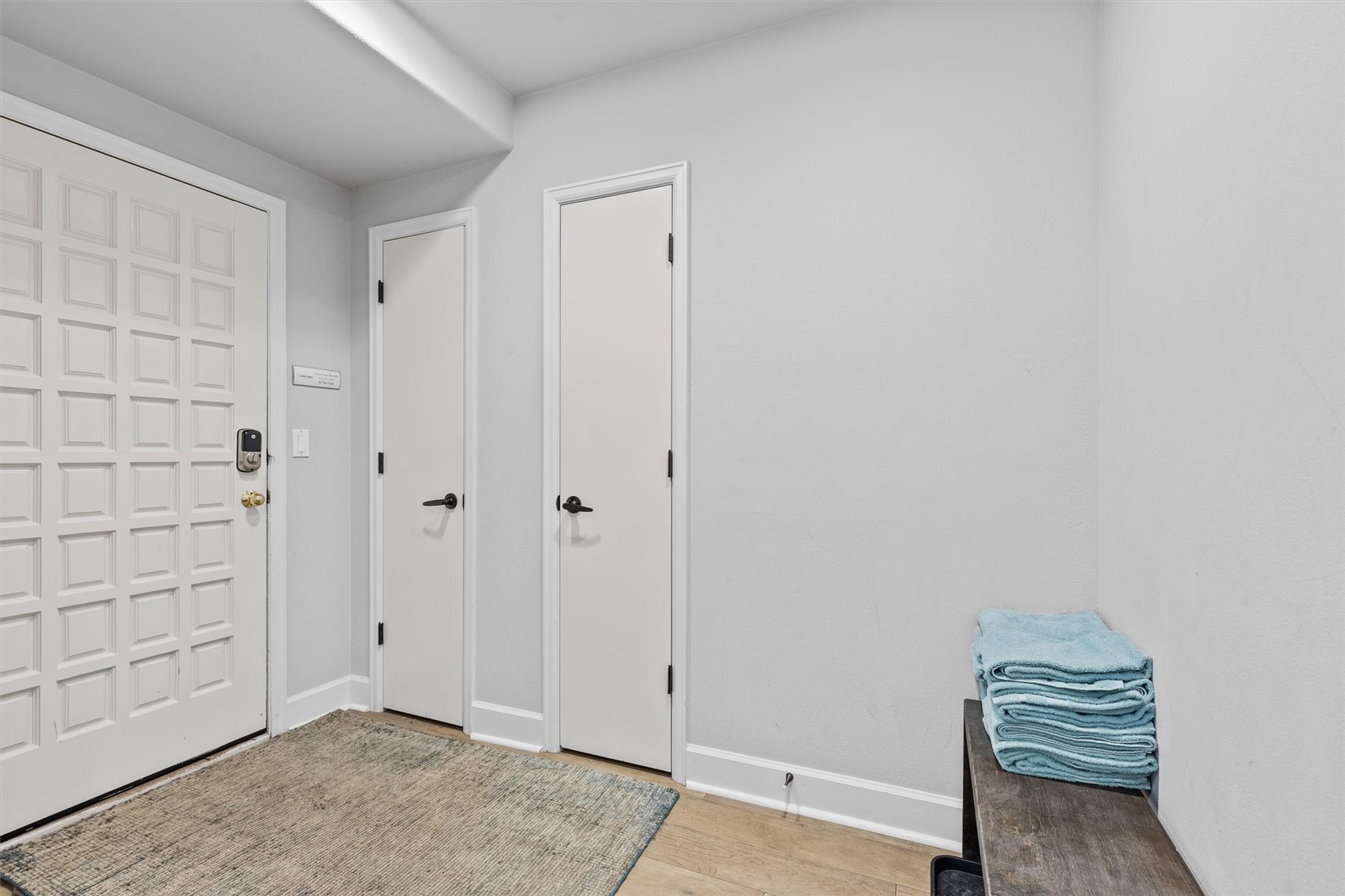 Entryway with a paneled front door, neutral woven rug, and folded blue towels on a bench.