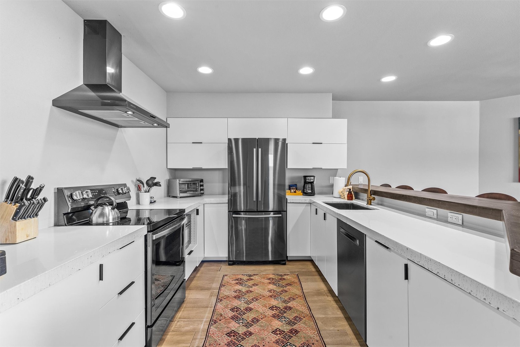 Modern white kitchen with stainless steel appliances, brass faucet, and patterned runner rug.