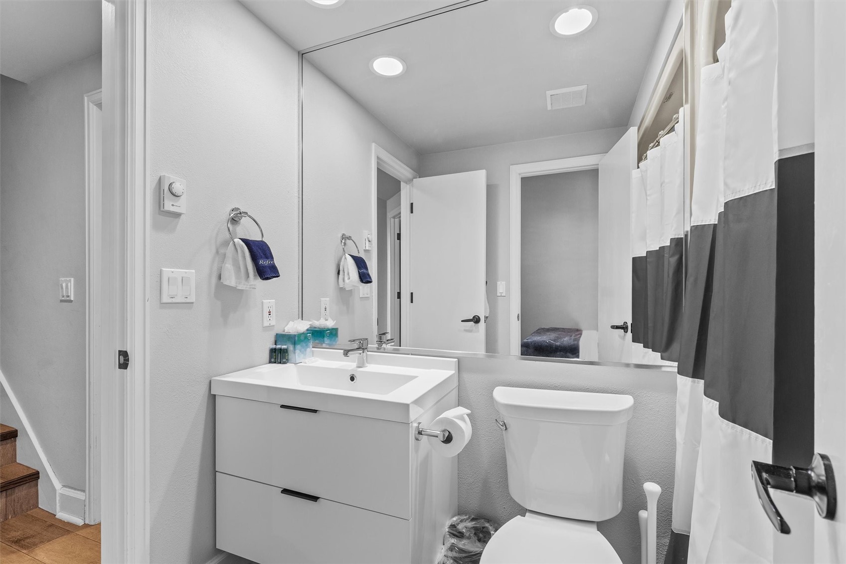 Bathroom with a white vanity, large mirror, toilet, and striped shower curtain.