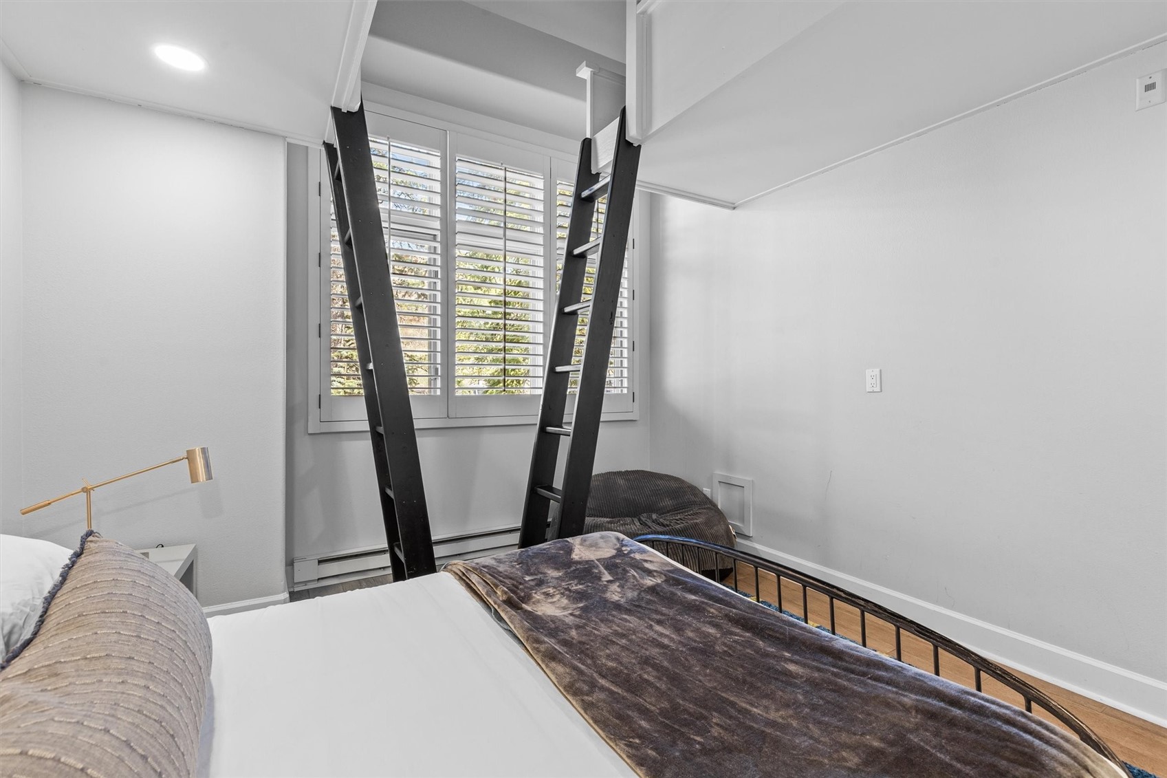 Bedroom with a black ladder leading to a loft bed and plantation shutters.