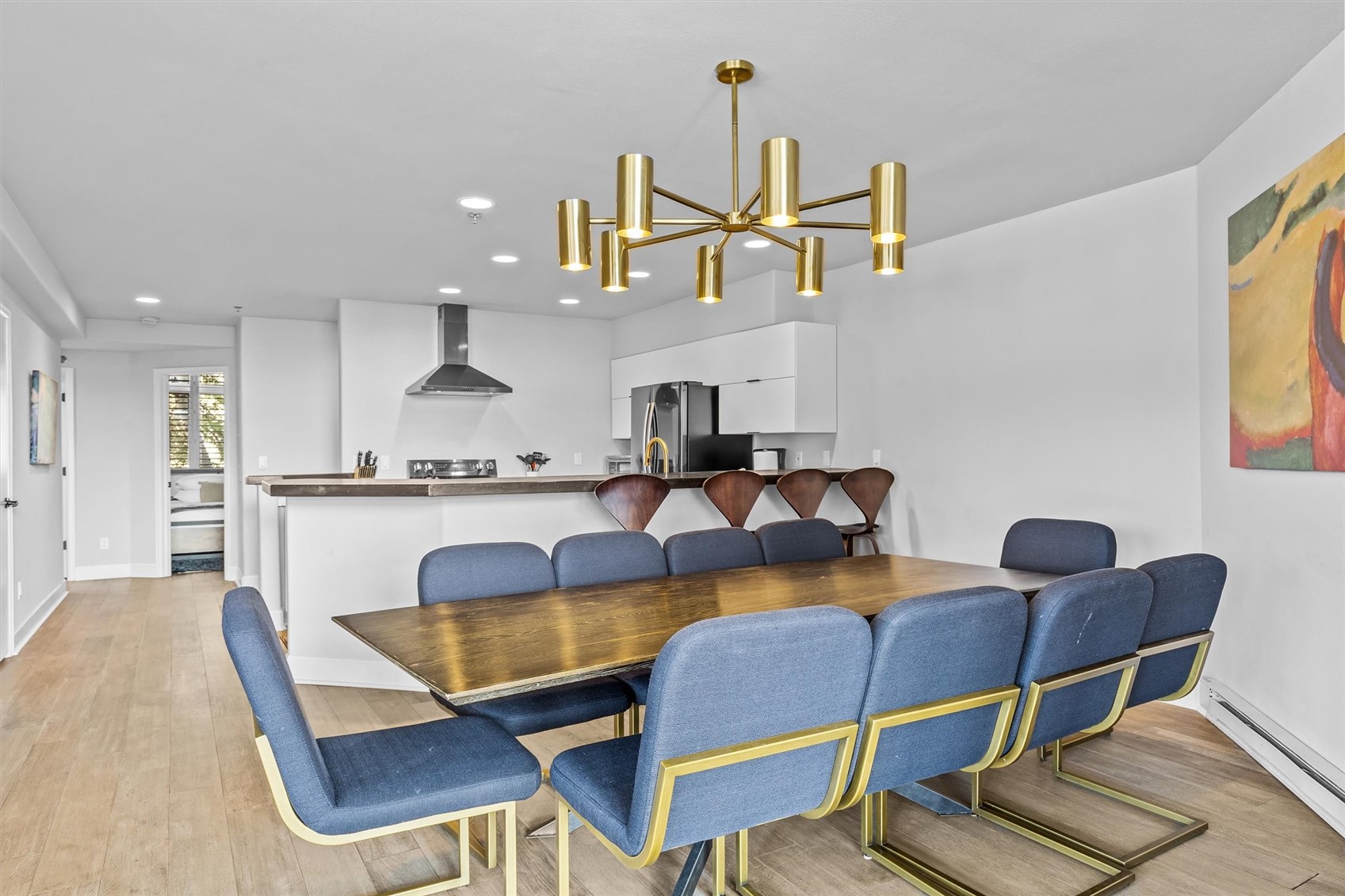 Dining area with a long wood table, blue and gold chairs, and an open kitchen.