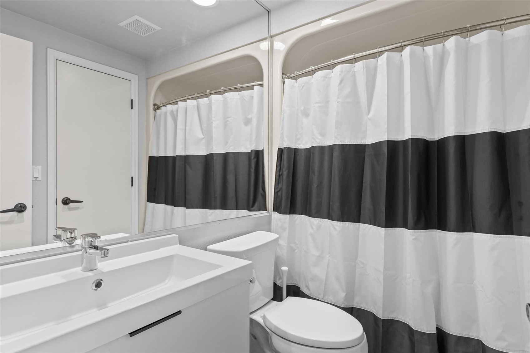Bathroom with a white vanity, toilet, and white-and-charcoal striped shower curtain.