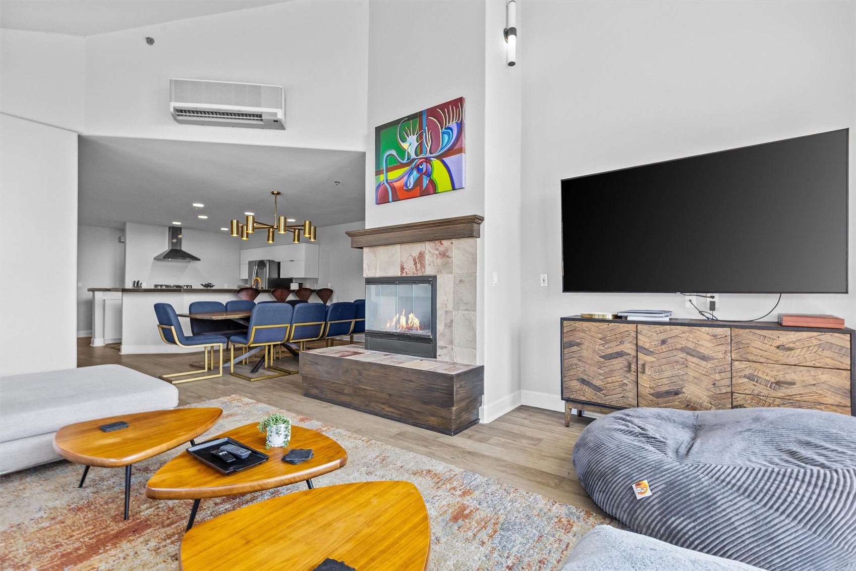 Furnished living room with a stone fireplace, large television, and open kitchen.