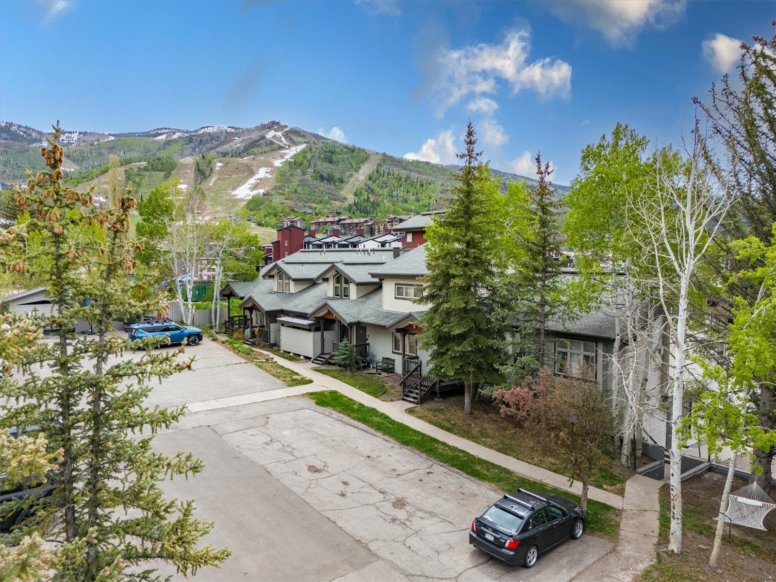 Aerial view of Ski Time Square residences beneath green ski slopes and snow-patched mountains.