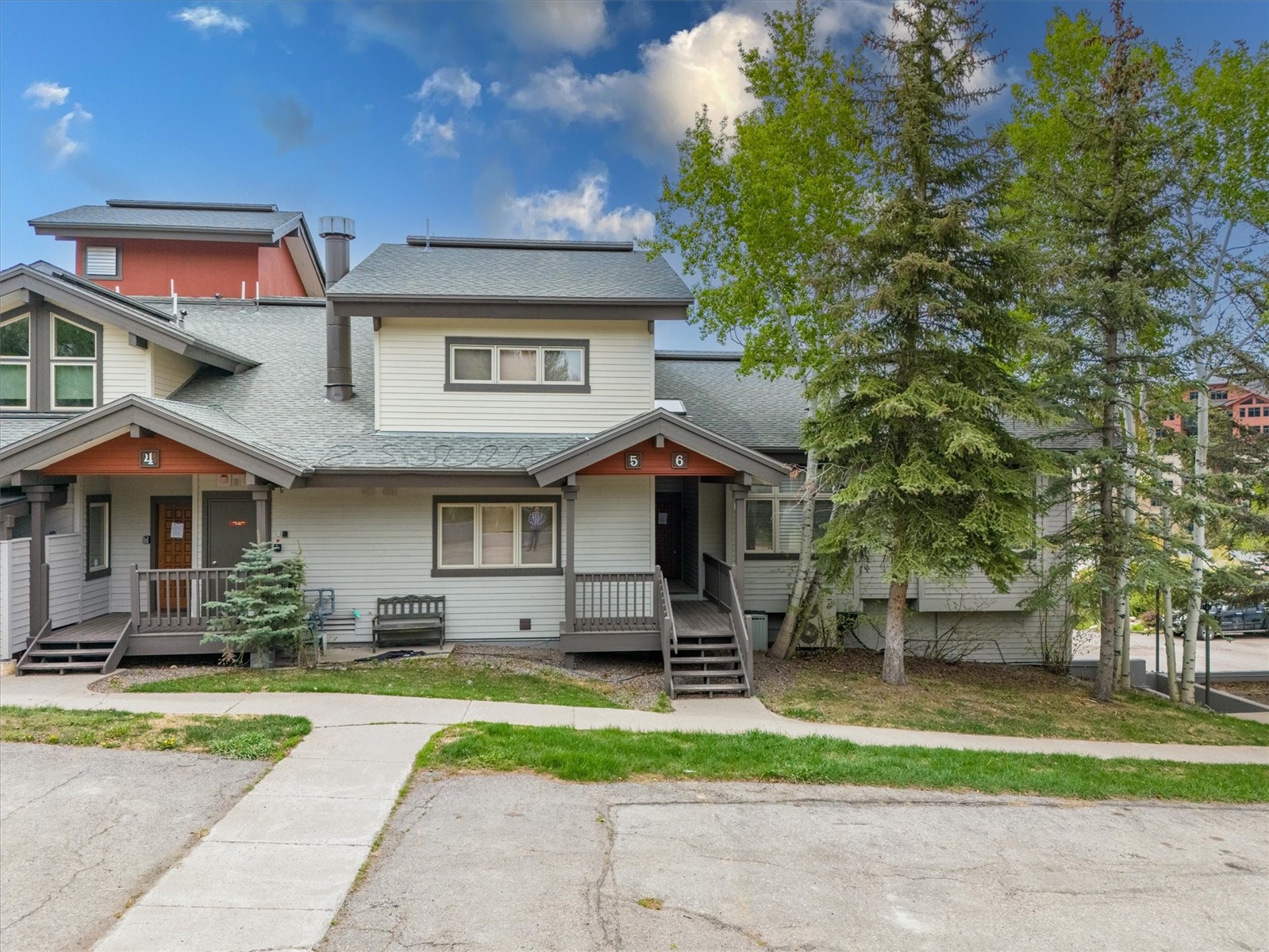Gray multi-unit building with numbered porch entrances and mature trees.