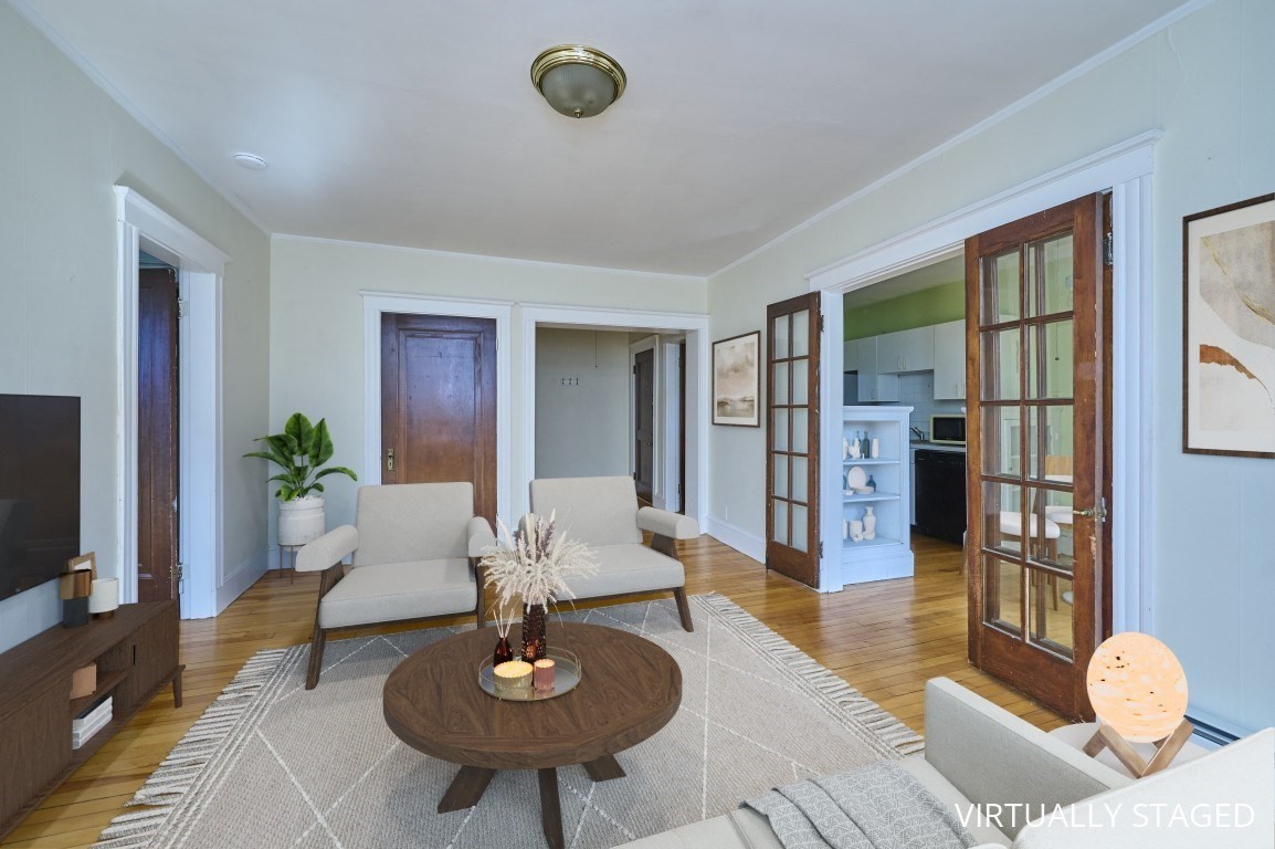 Virtually staged living room with hardwood floors, a round coffee table, and French doors to the kitchen.