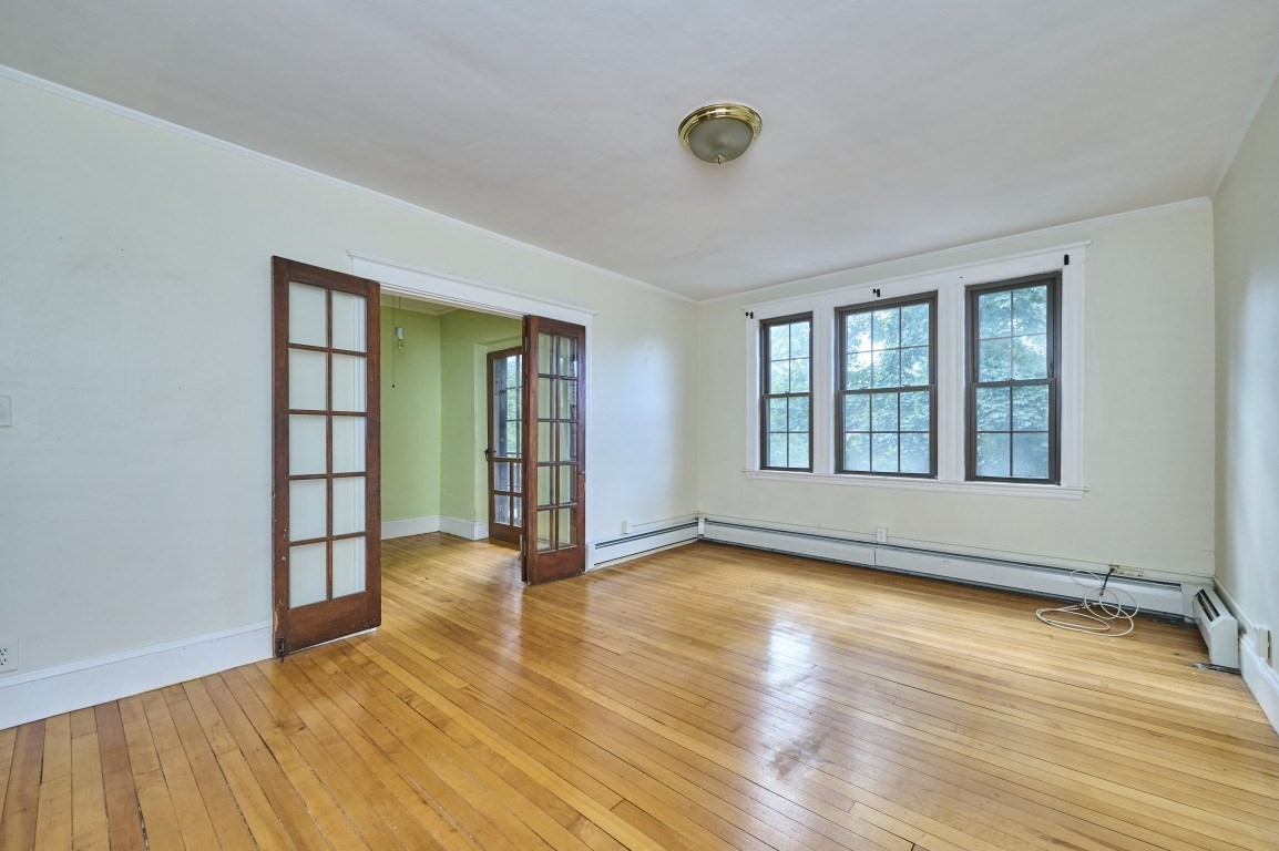 Empty room with hardwood floors, three windows, and open French doors.