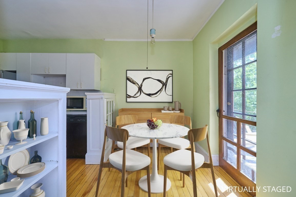 Dining area with a round white table, wooden chairs, hardwood floors, and a glass-paneled door.