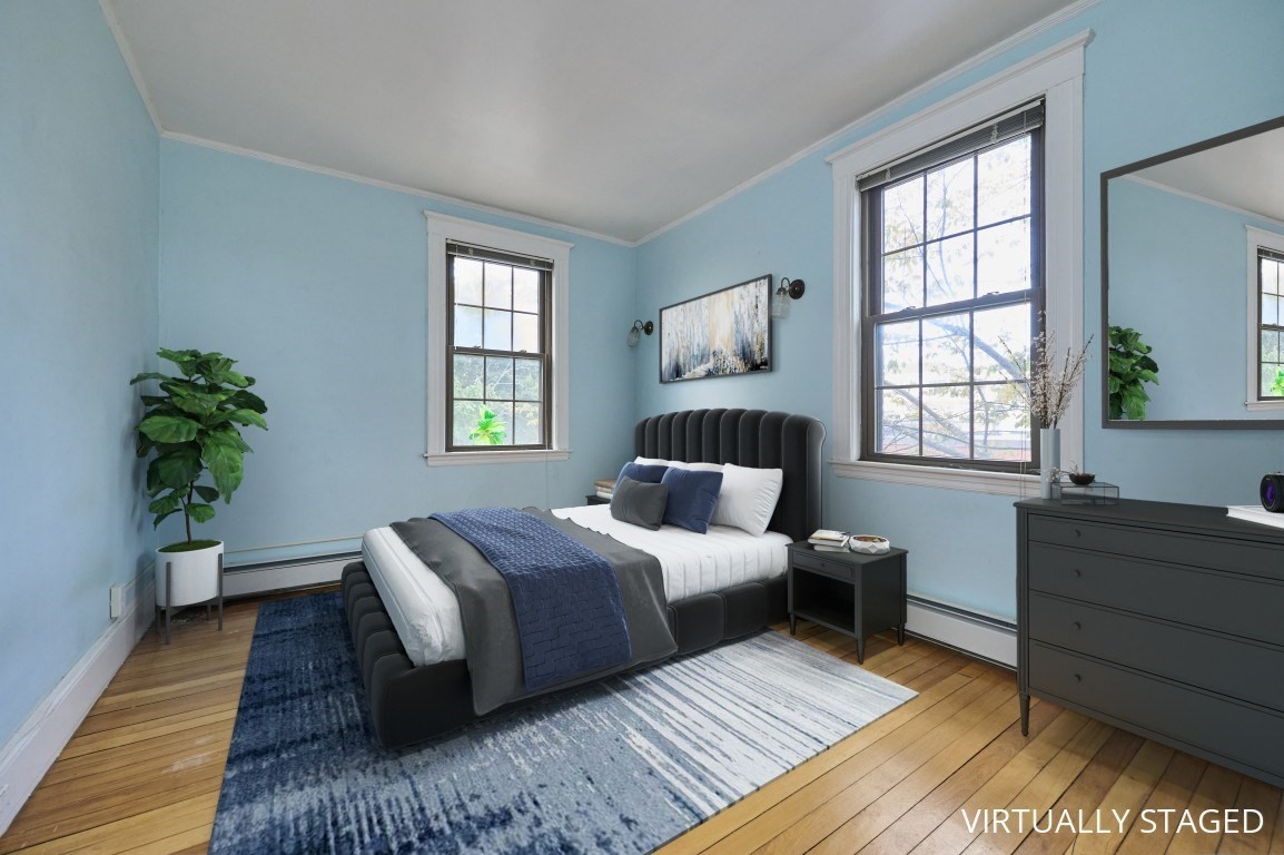 Bedroom with a dark upholstered bed, blue walls, hardwood floors, and two tall windows.