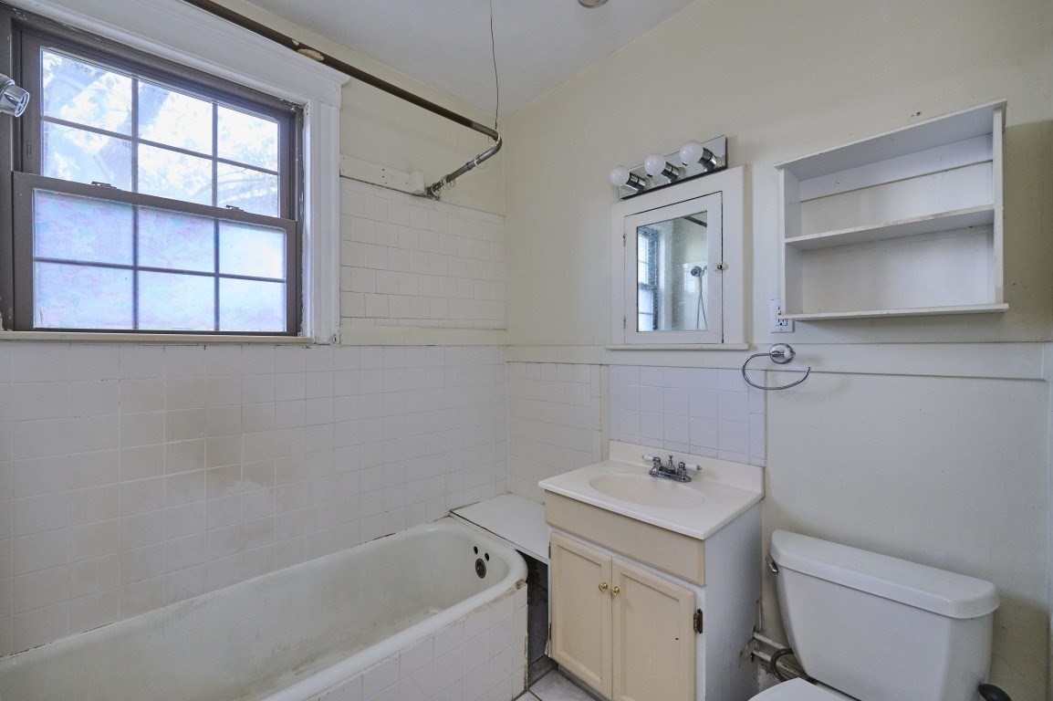 Bathroom with a bathtub beneath a large window, white tile, a sink vanity, and open wall shelving.