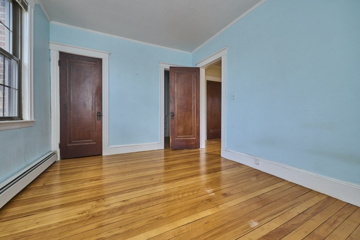 Empty room with blue walls, hardwood floors, dark wood doors, and a tall window.