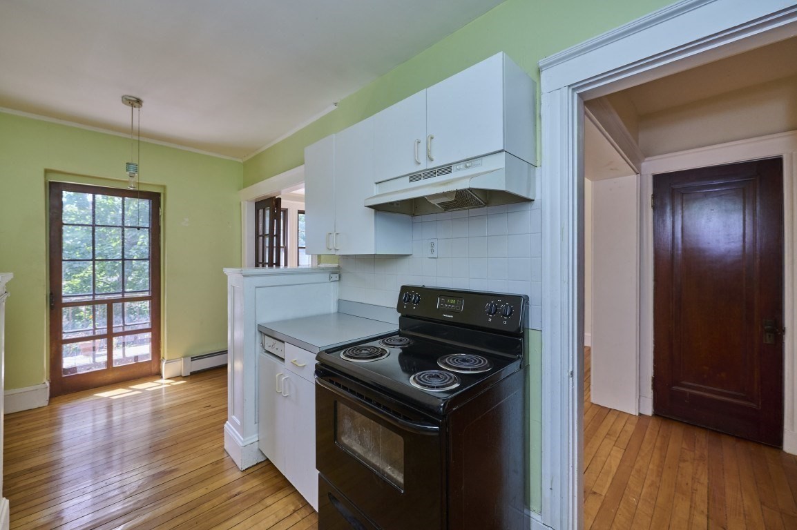 Kitchen with white cabinets, black electric range, pale green walls, and hardwood floors.