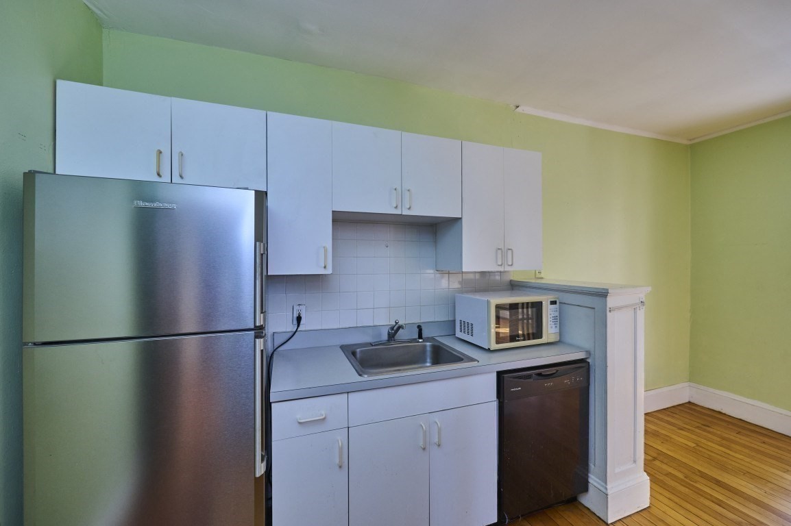 Compact kitchen with pale blue cabinets, stainless steel refrigerator, sink, microwave, and dishwasher.