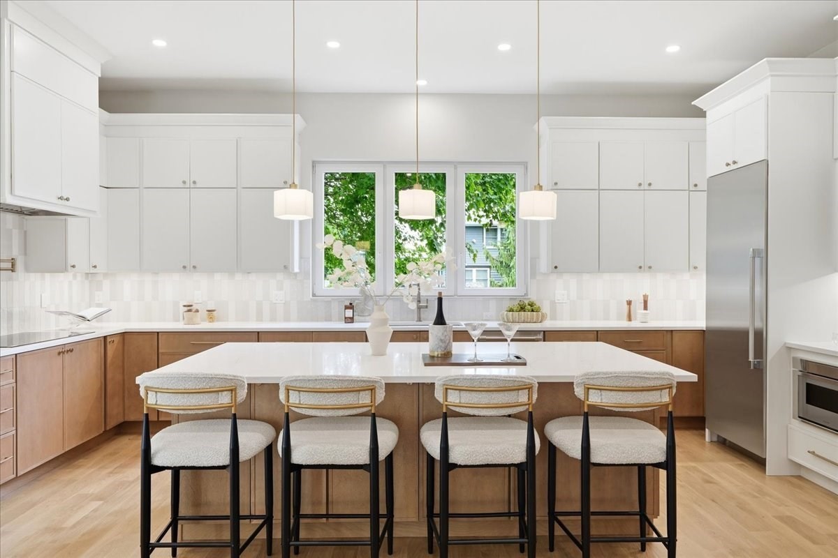 Bright kitchen with a large white island, four bar stools, and a wide window above the sink.