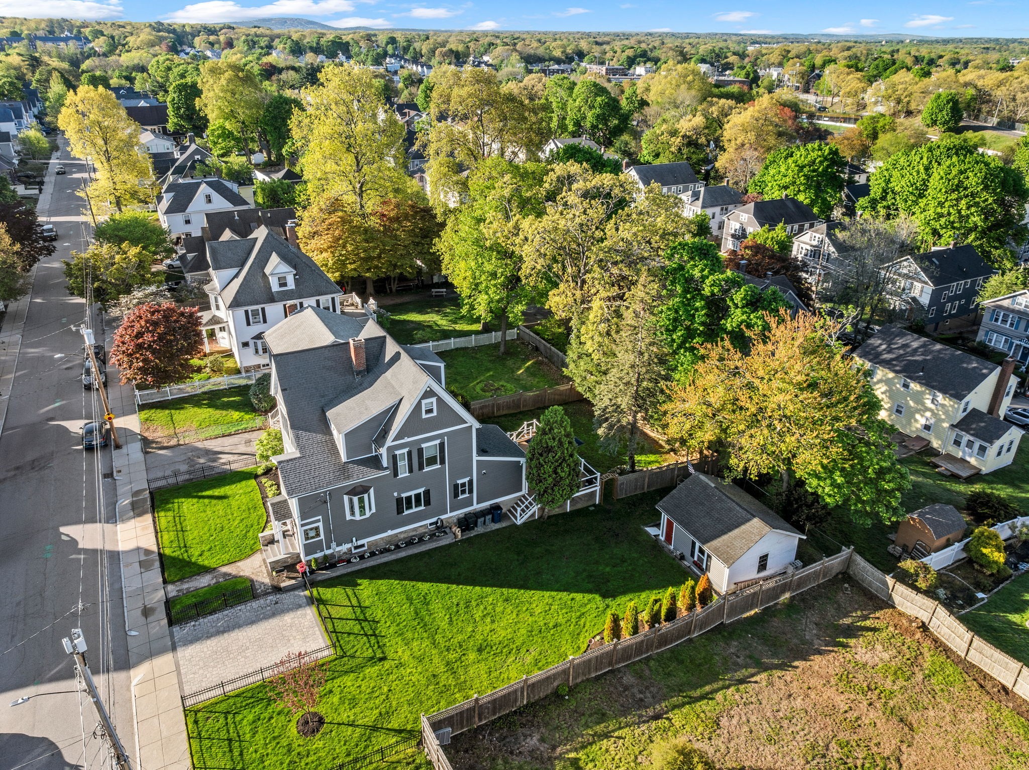 Aerial view of a gray house with a large fenced lawn in a tree-lined neighborhood.