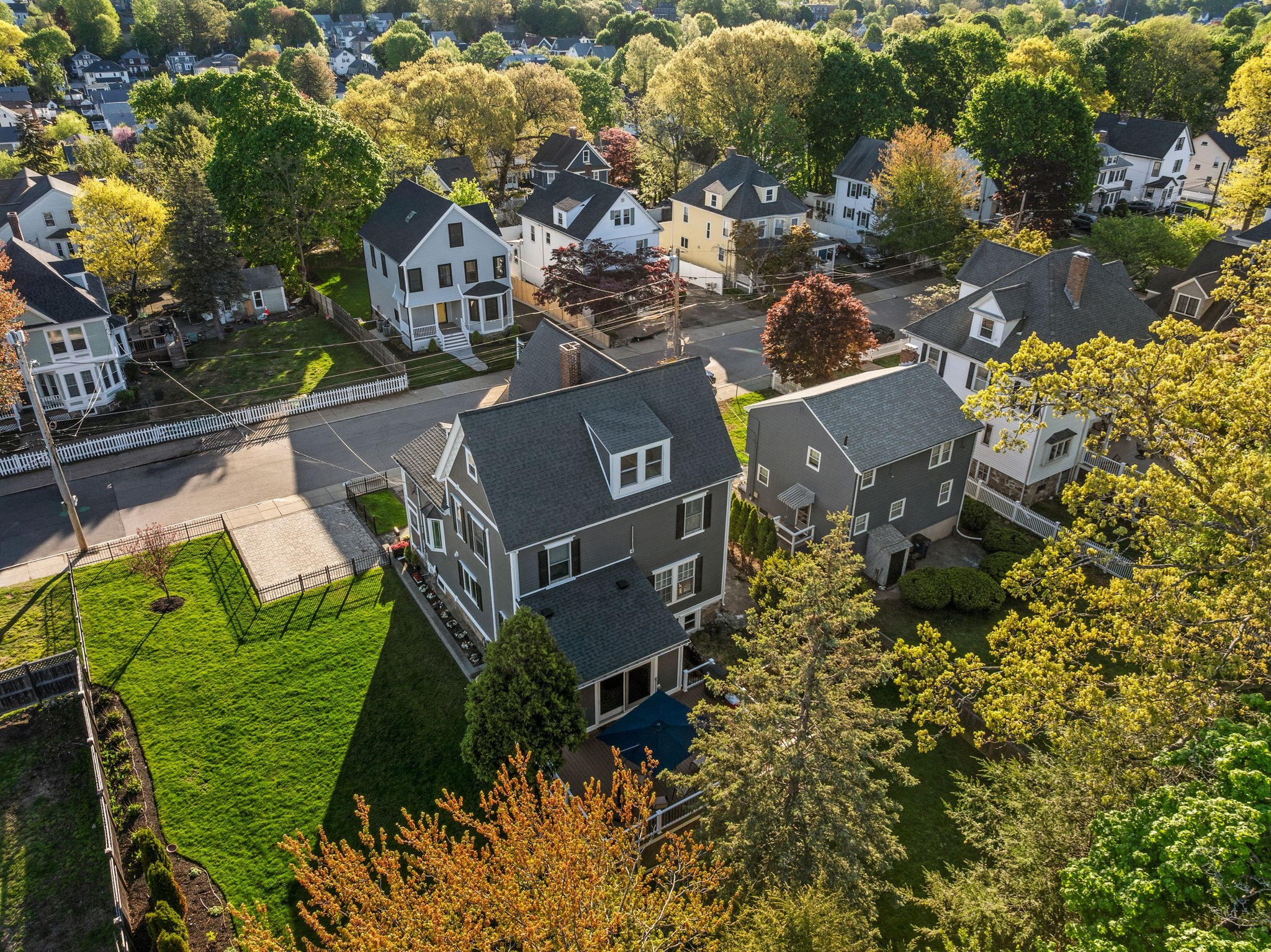Gray multi-story house with a dark roof and large fenced green yard, viewed from above.
