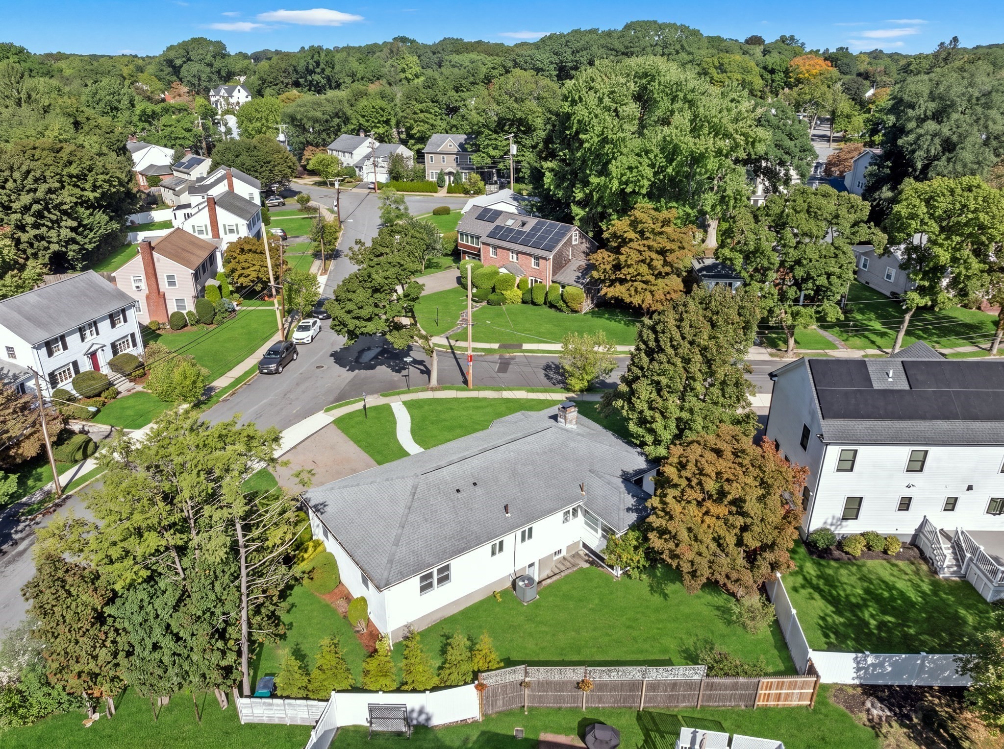 Aerial view of a white home and fenced green backyard among tree-lined neighborhood streets.
