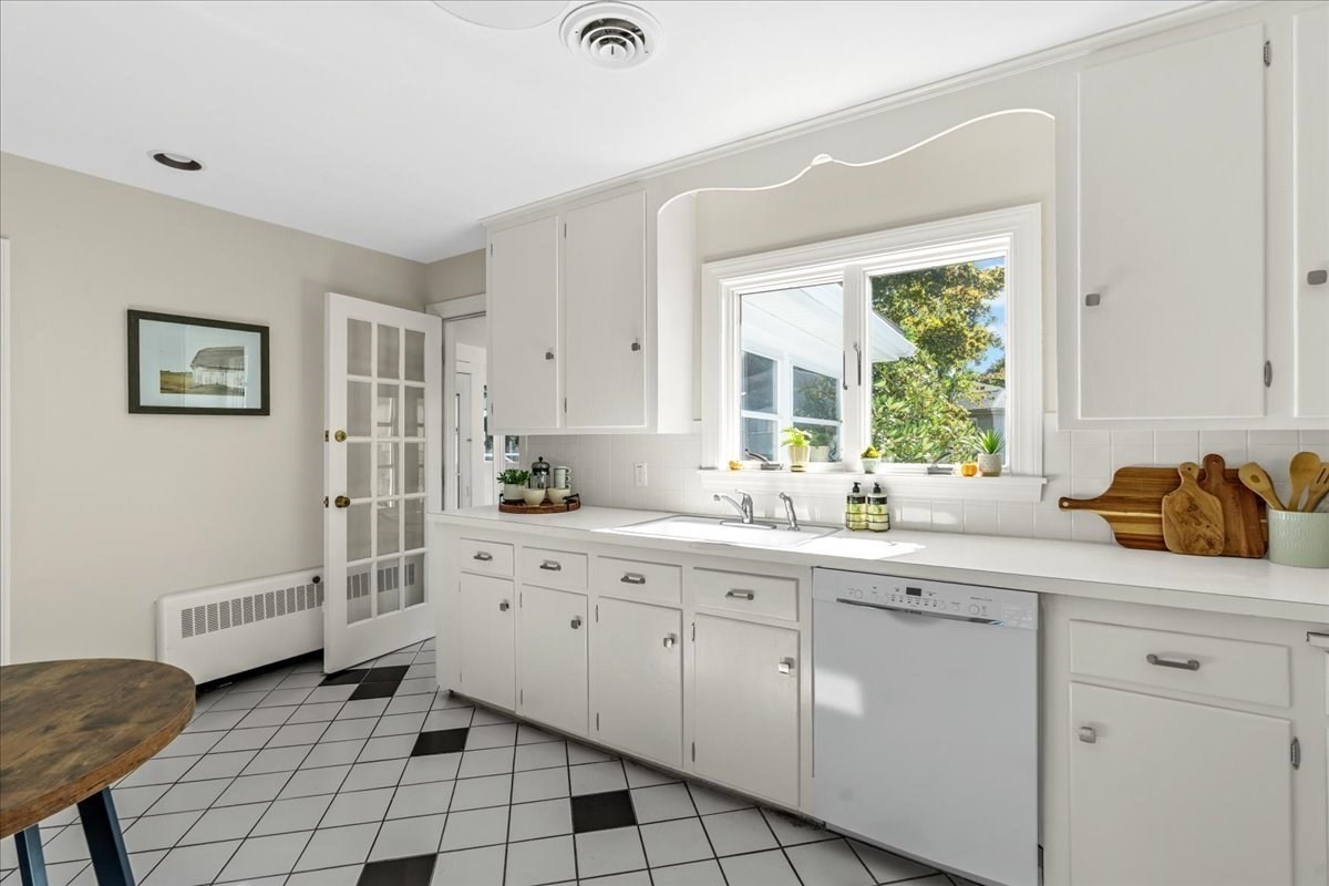 White kitchen with paneled cabinets, a sink beneath a sunny window, and black accent tiles in the floor.