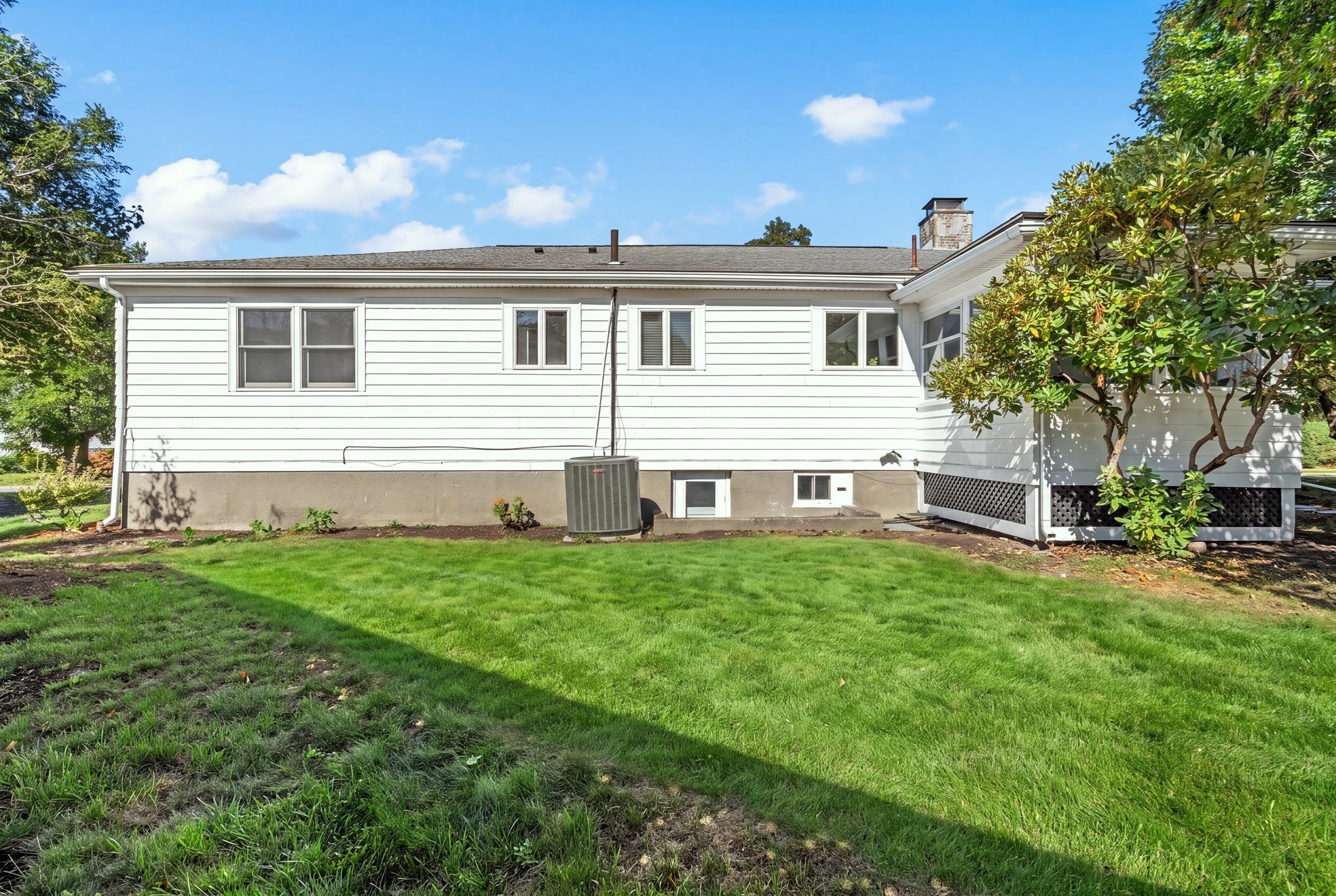 Rear of a white-sided house with an outdoor HVAC unit and broad green lawn.