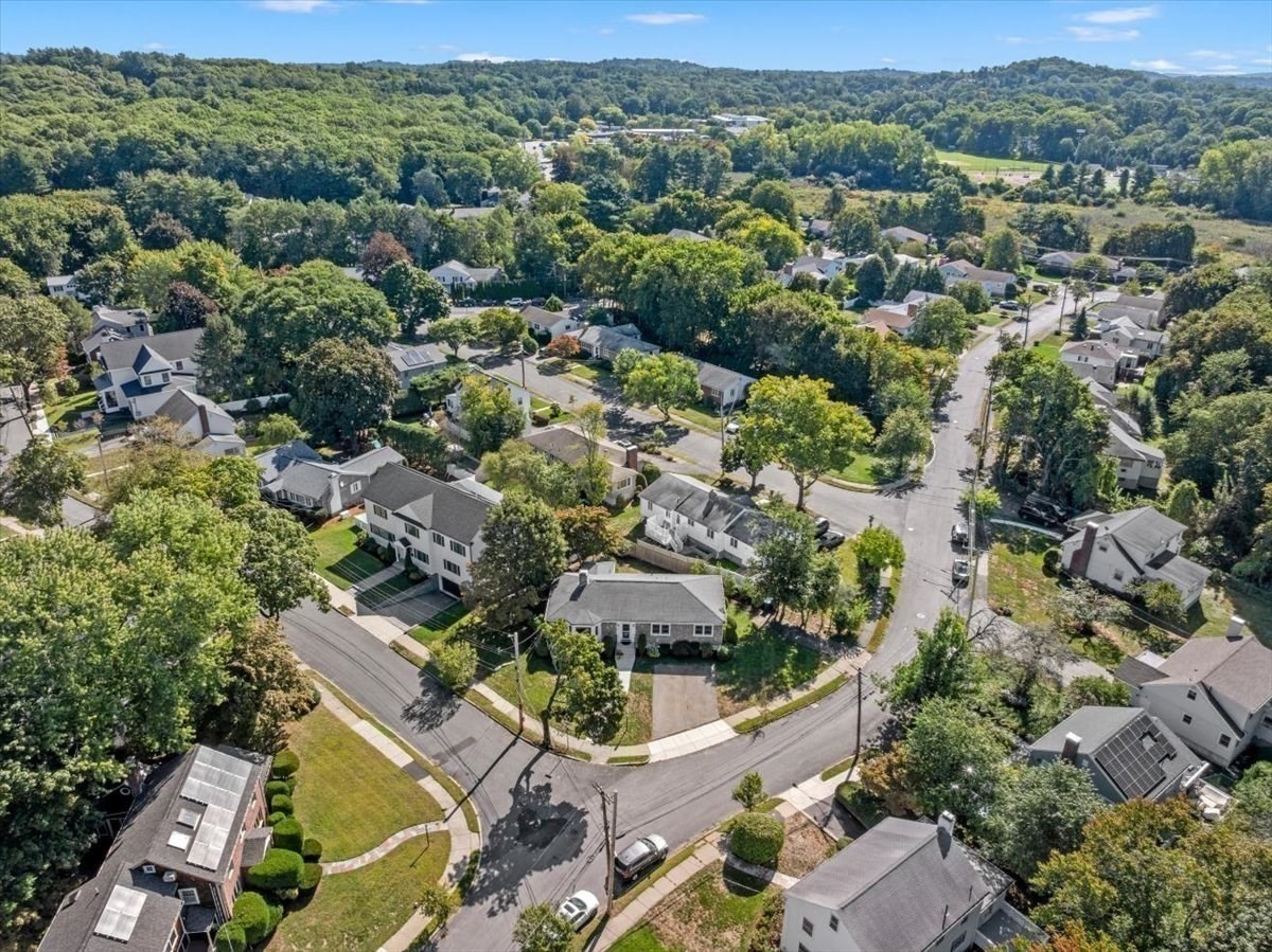 Aerial view of a leafy neighborhood with homes, intersecting streets, and wooded hills.