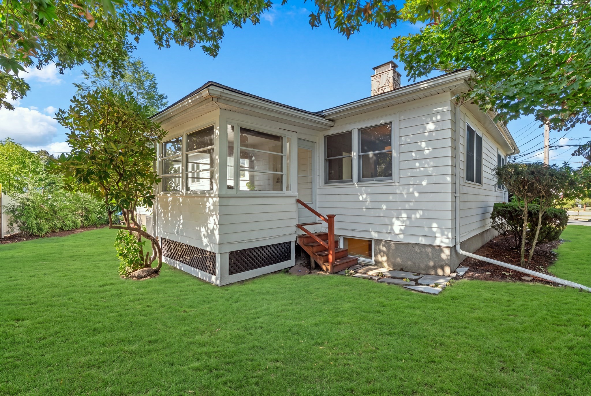 White-sided house with an enclosed porch and wooden steps overlooking a broad green lawn.