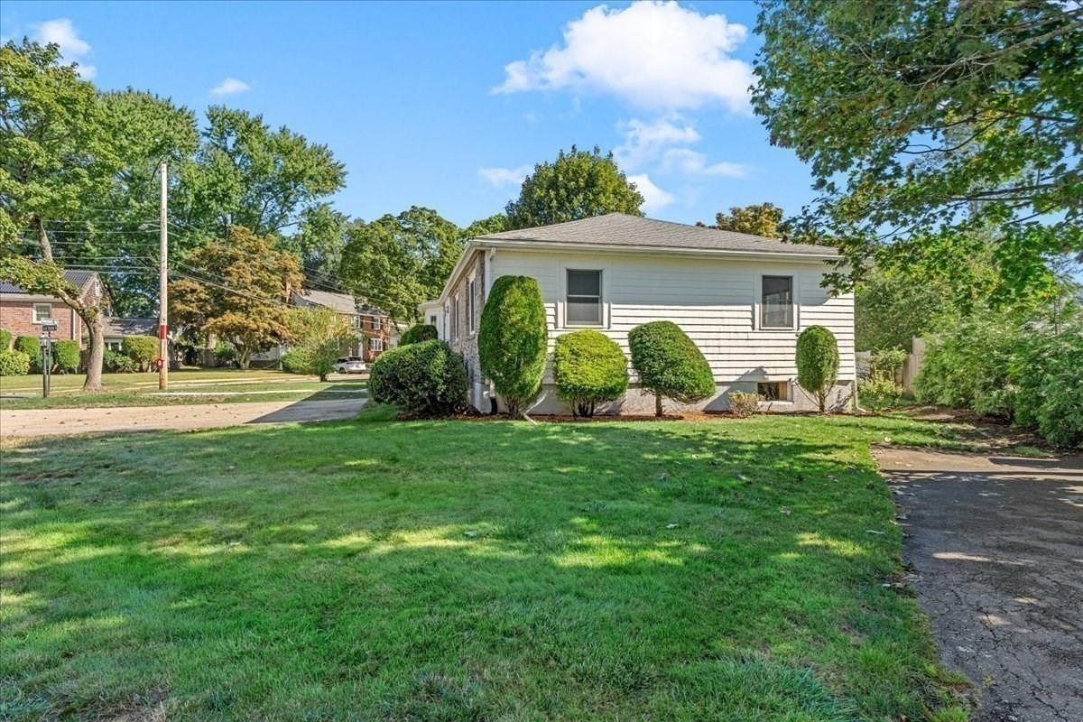 Single-story light-sided home with trimmed shrubs, a broad lawn, and a driveway.