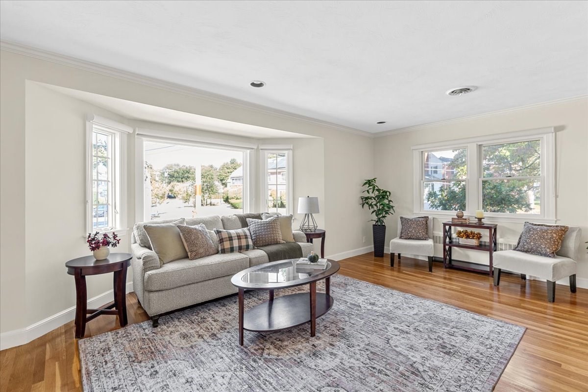 Staged living room with a gray sofa, patterned rug, and large windows.