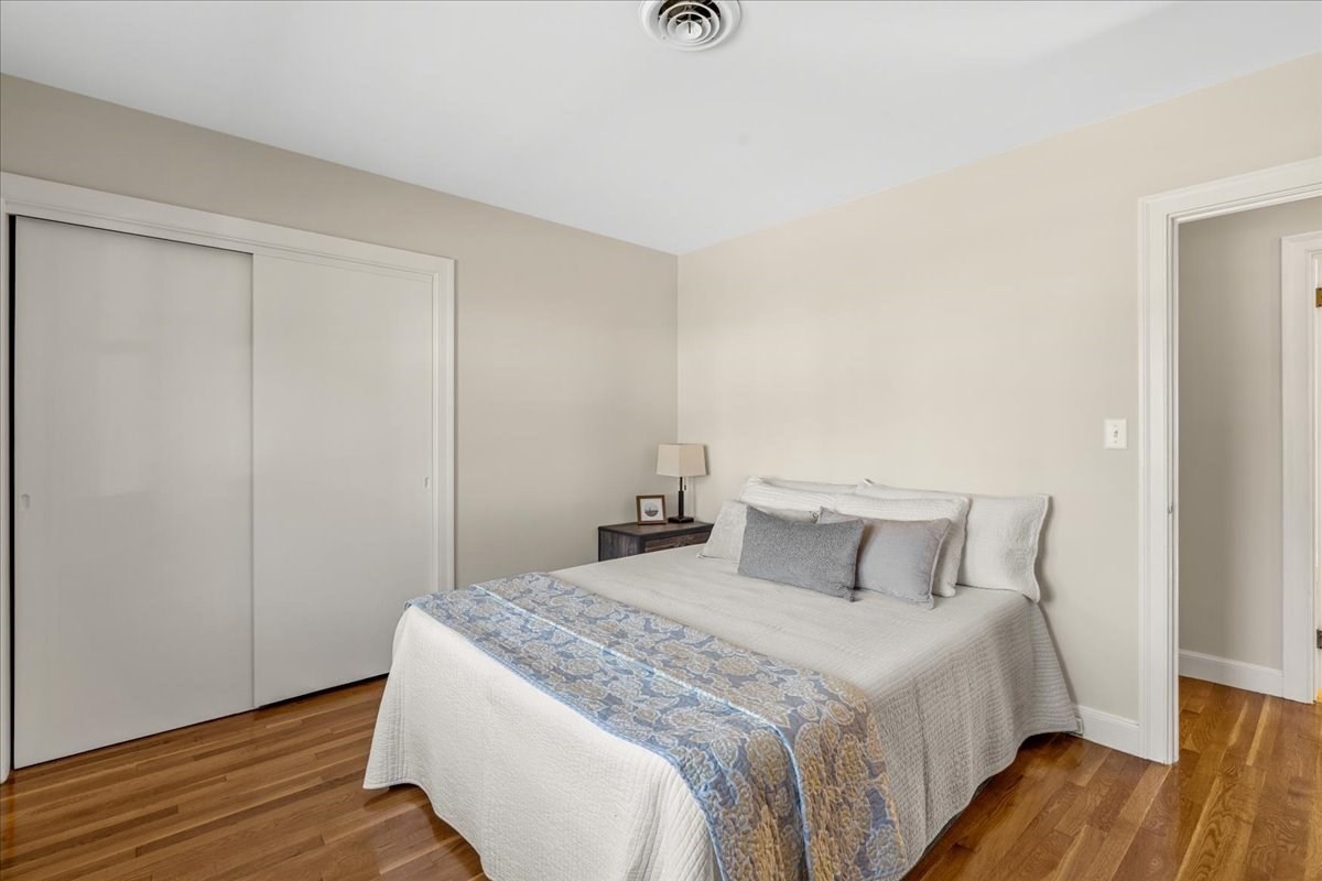 Bedroom with a white quilted bed, blue patterned runner, sliding-door closet, and hardwood floor.