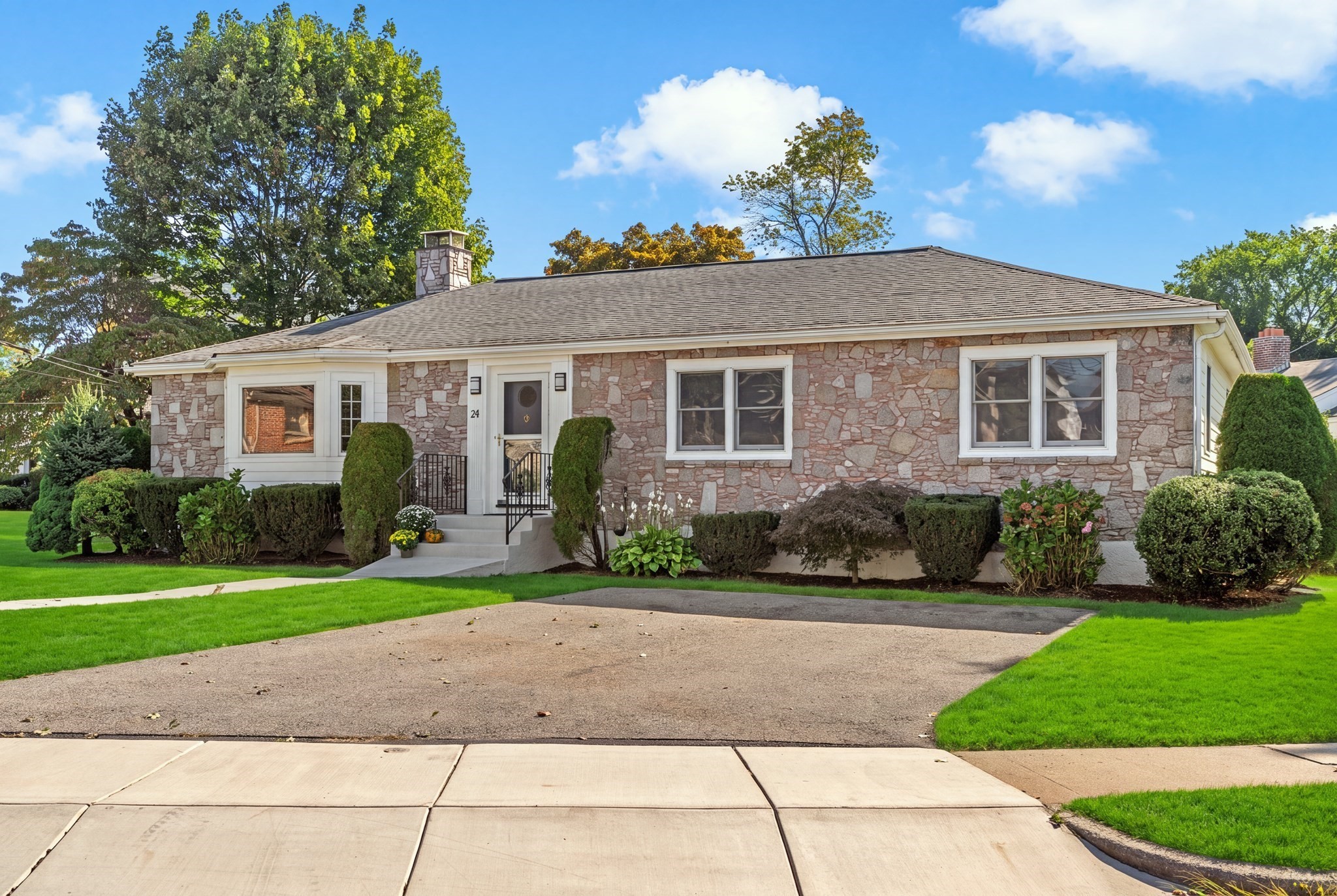 Single-story stone-faced home with a broad driveway and manicured shrubs.