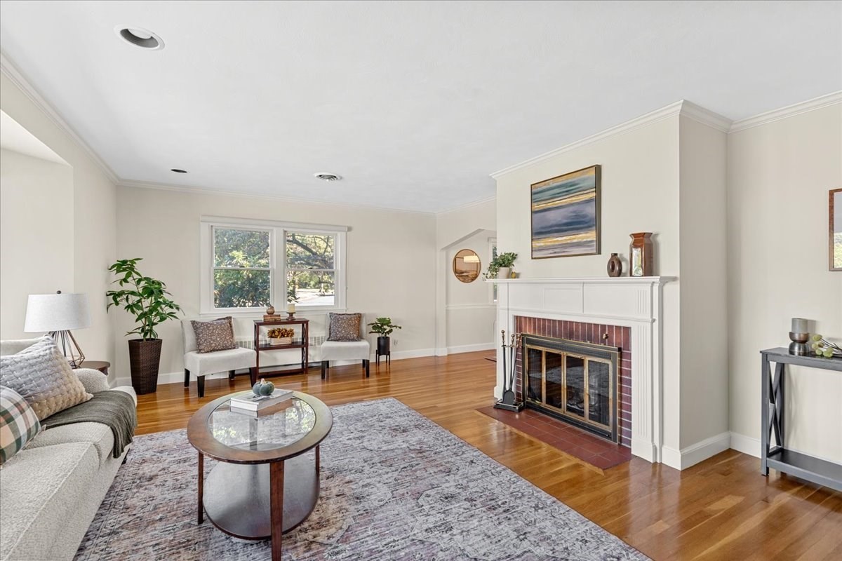 Living room with a brick fireplace, hardwood floors, and seating beside two windows.