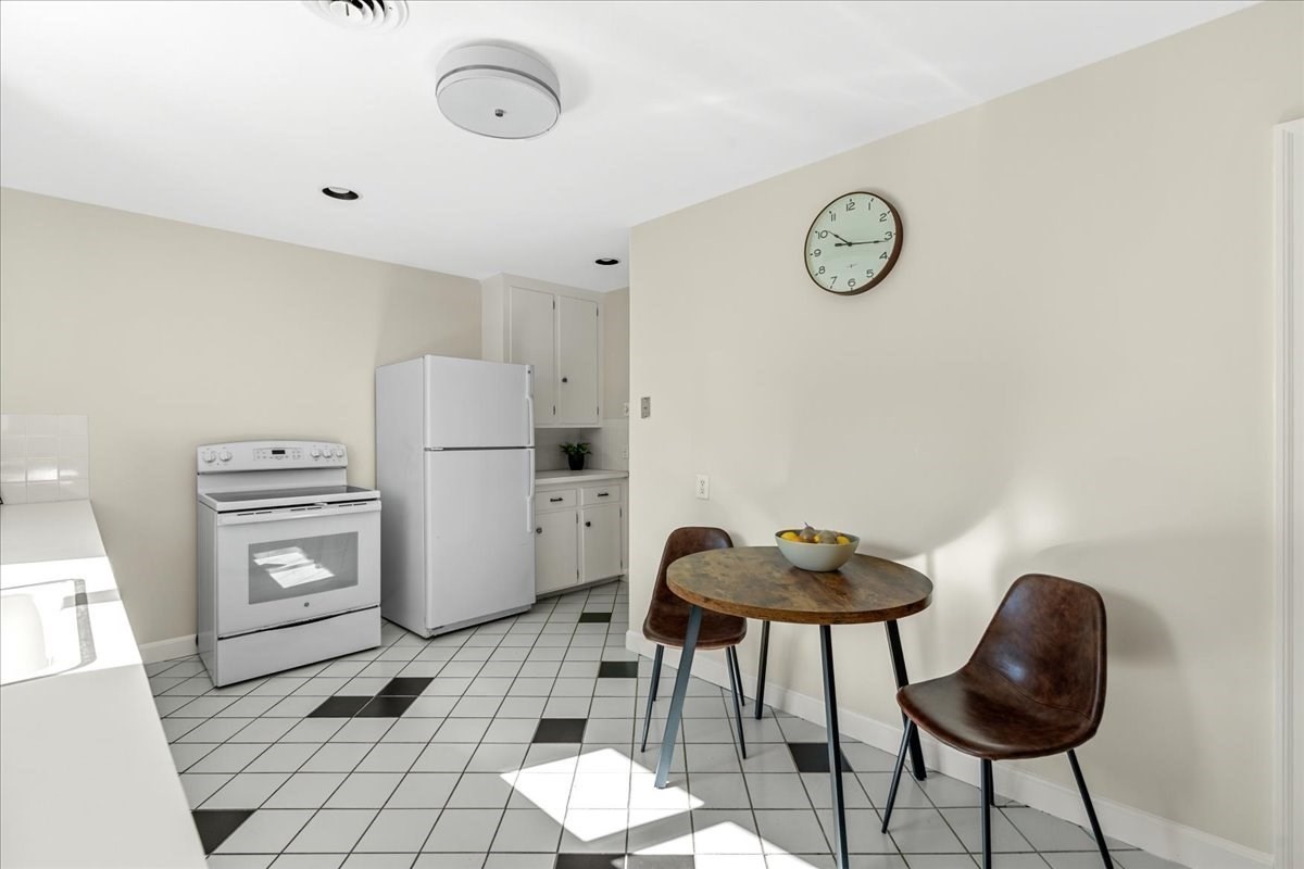 Compact kitchen with white appliances, patterned tile floor, and a round table with two chairs.