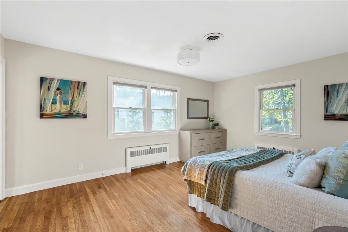 Bedroom with blue-and-white bedding, hardwood floors, two windows, and colorful wall art.