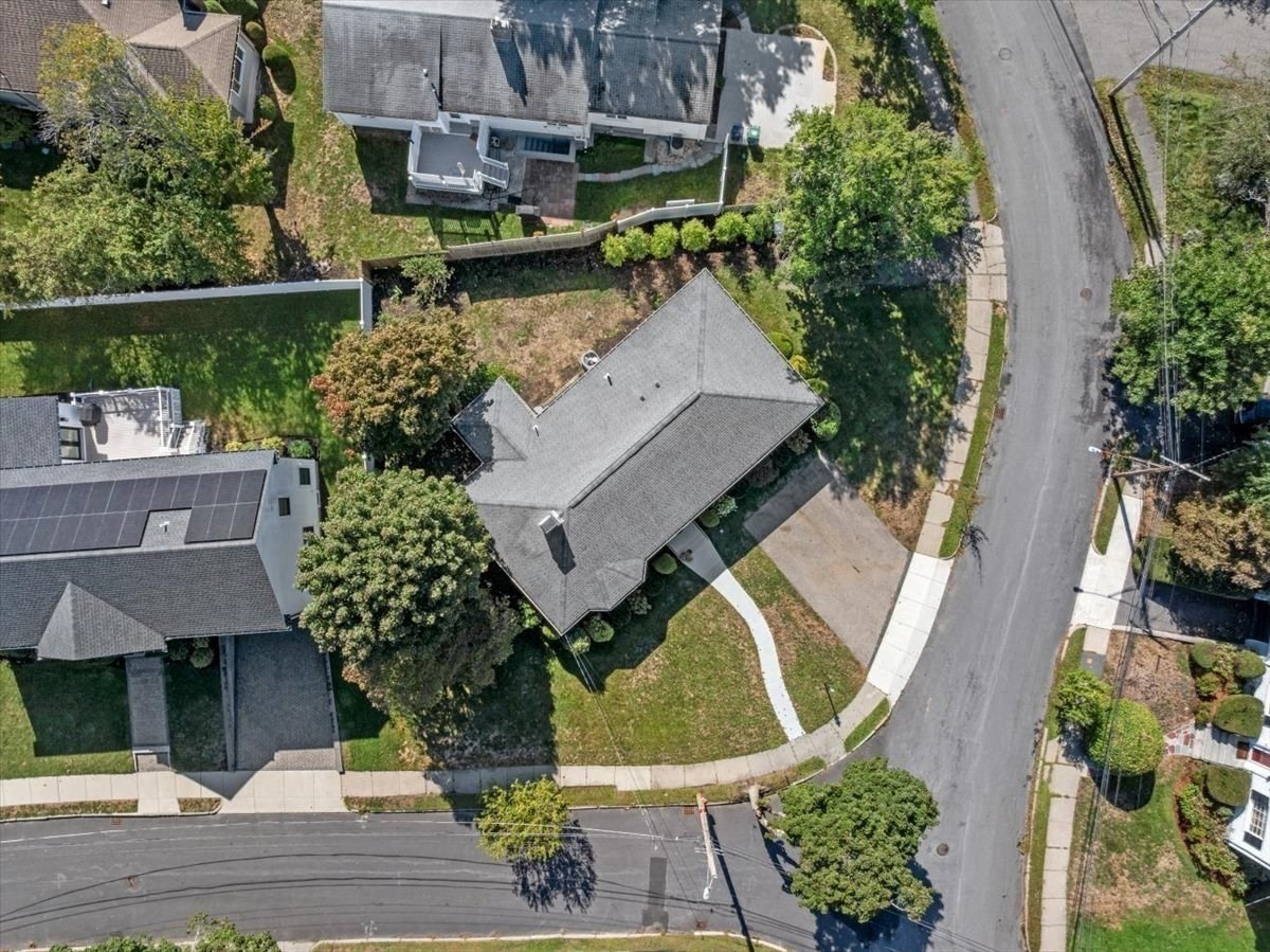 Aerial view of a gray-roofed home on a landscaped corner lot with a curved driveway.