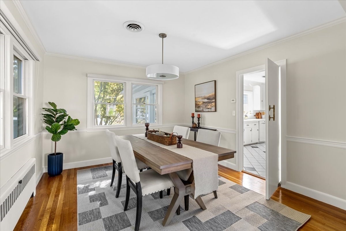 Dining room with a wooden table, geometric rug, hardwood floors, and large windows.