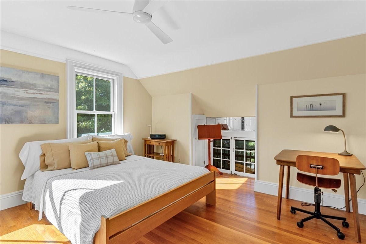 Bedroom with a vaulted ceiling, wooden bed, desk, and sunlit hardwood floors.