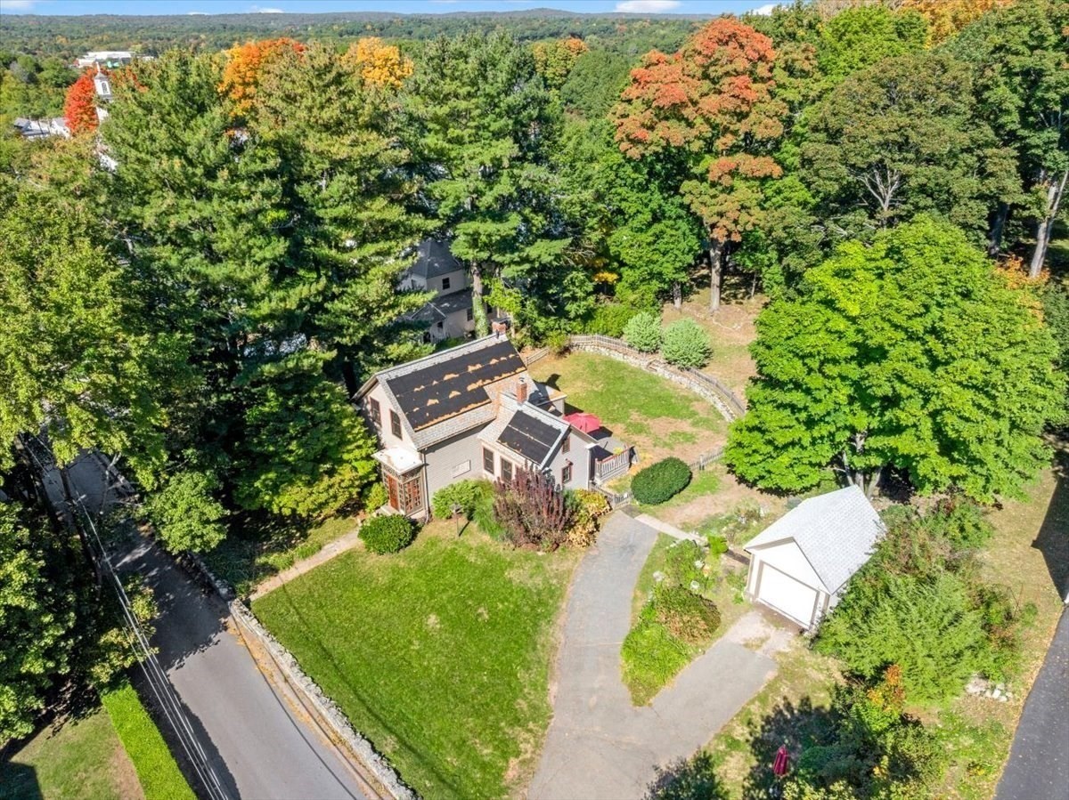 Aerial view of a house surrounded by mature trees, with a broad lawn, curved driveway, and detached garage.