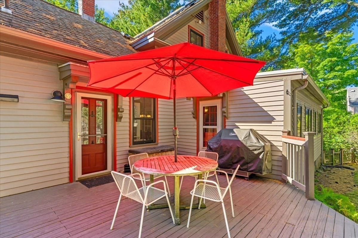 Wooden backyard deck with a round dining set beneath a bright red umbrella and a covered grill.