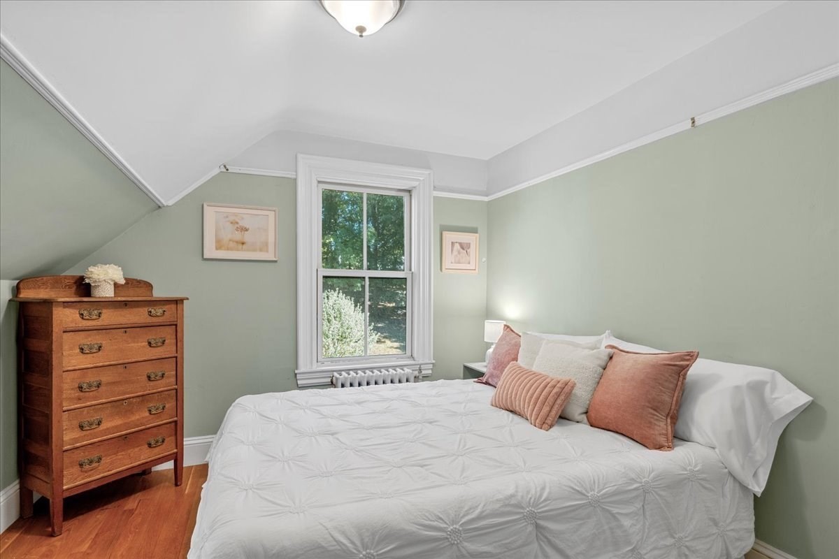 Bedroom with a sloped ceiling, sage-green walls, a white bed, and a wood dresser beside the window.