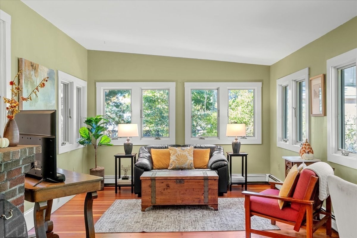 Living room with green walls, large windows, hardwood floors, and a brick fireplace.