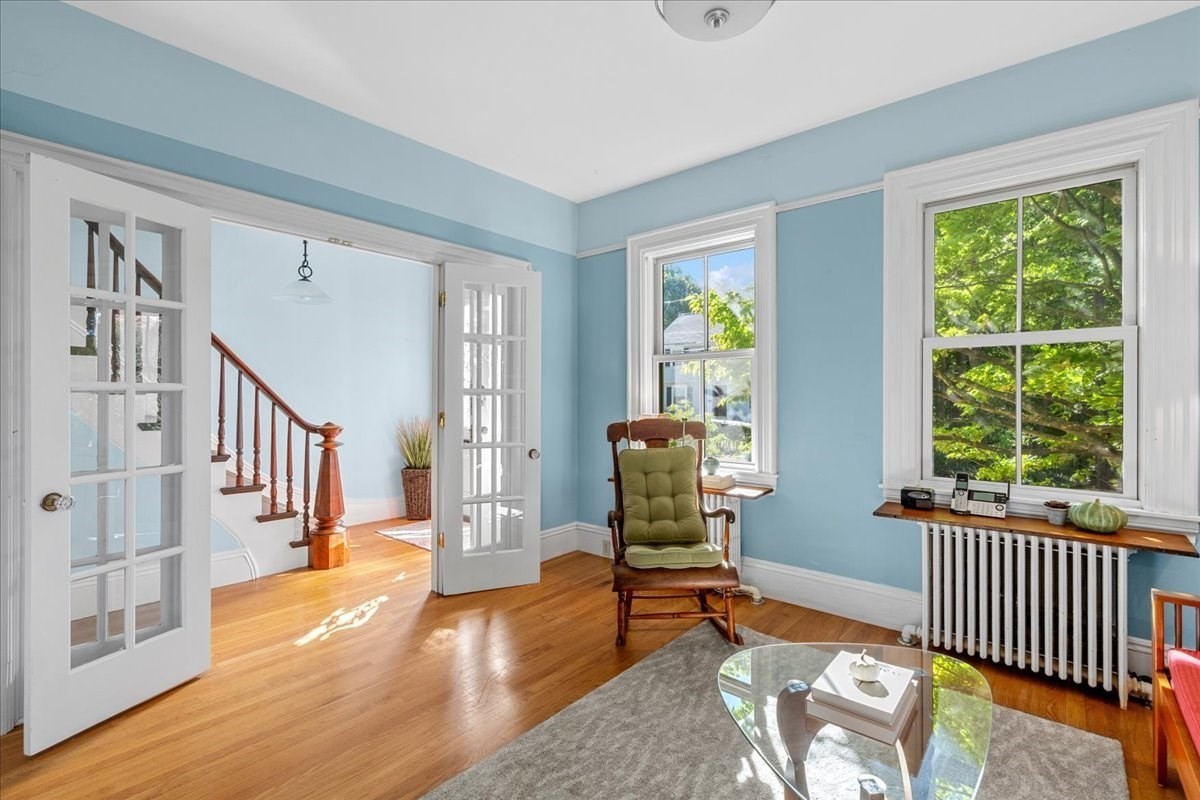 Living room with blue walls, French doors, hardwood floors, and windows overlooking leafy trees.
