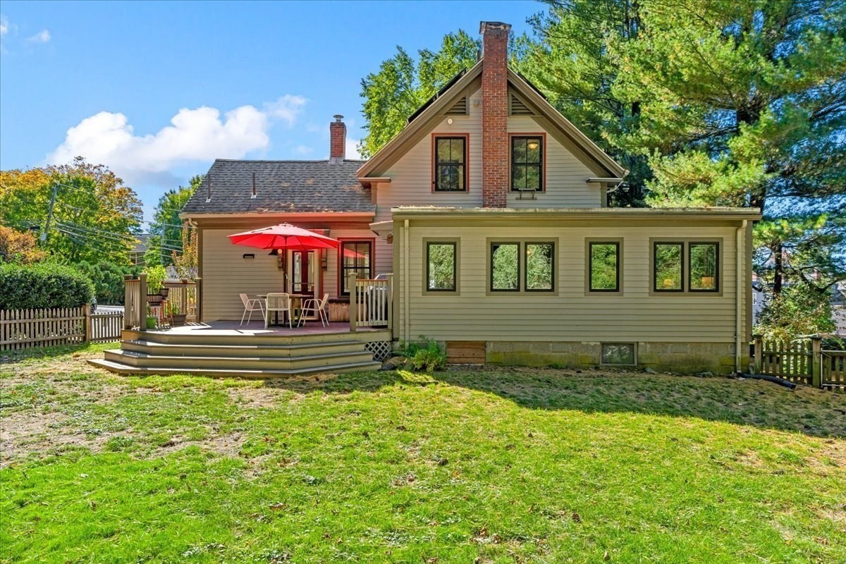 Rear exterior of a two-story home with a raised deck, red umbrella, and broad lawn.