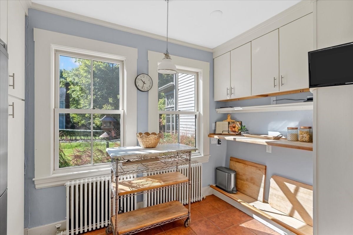Kitchen with white cabinets, wooden shelves, and a rolling island between two large windows.