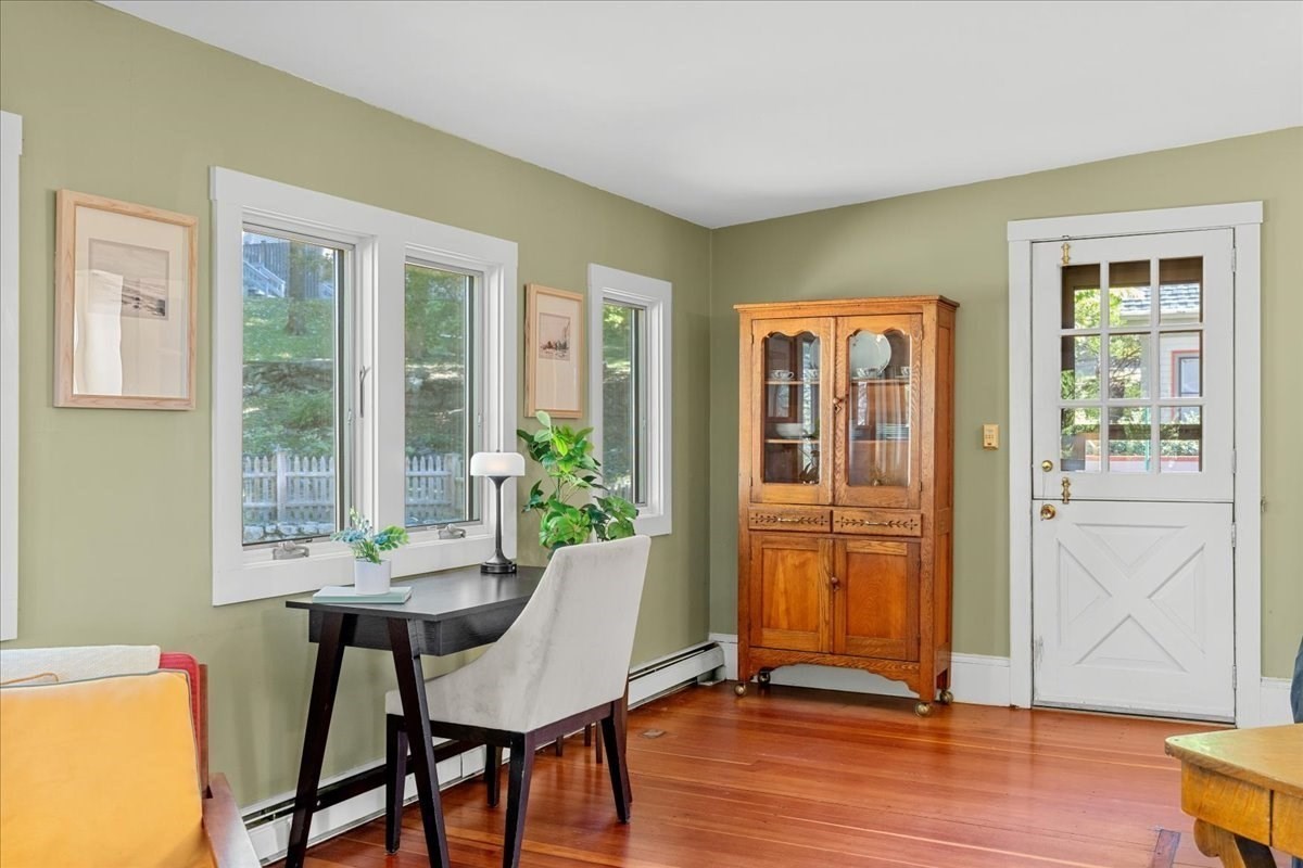 Furnished room with a desk beneath windows, a wooden cabinet, and a white divided-light door.