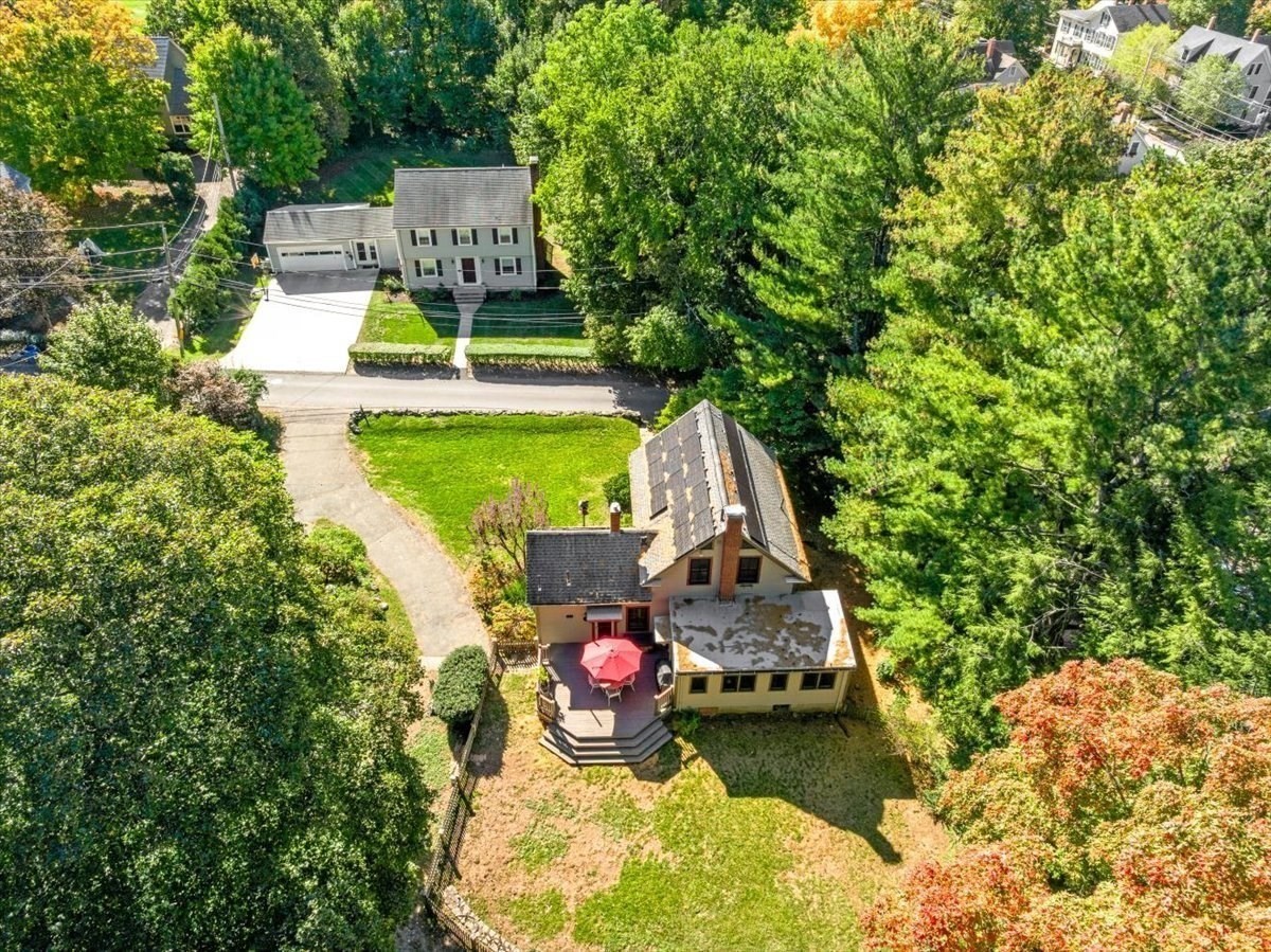 Aerial view of home with a red patio umbrella and mature surrounding trees.