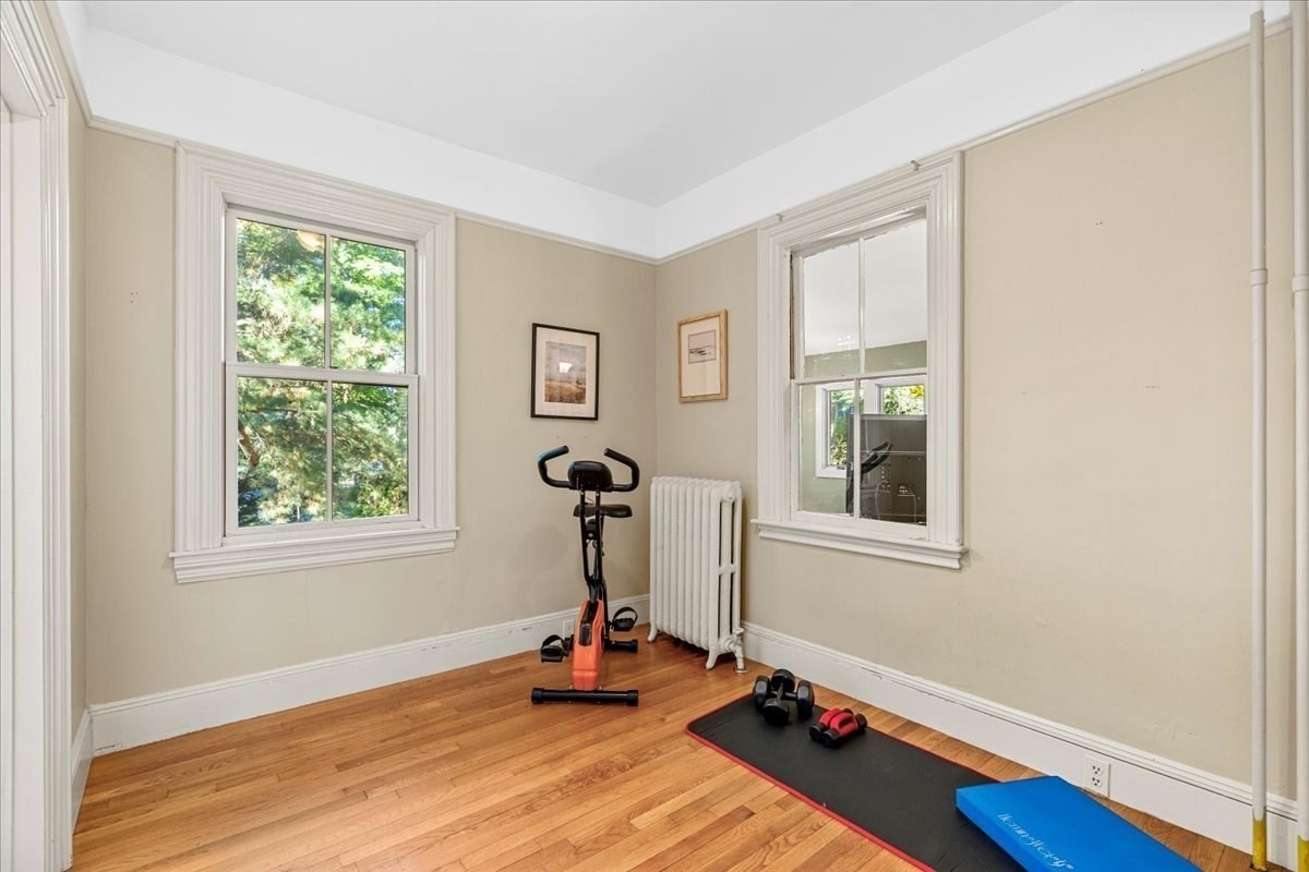 Home workout room with an exercise bike, dumbbells, and a mat on hardwood floors.